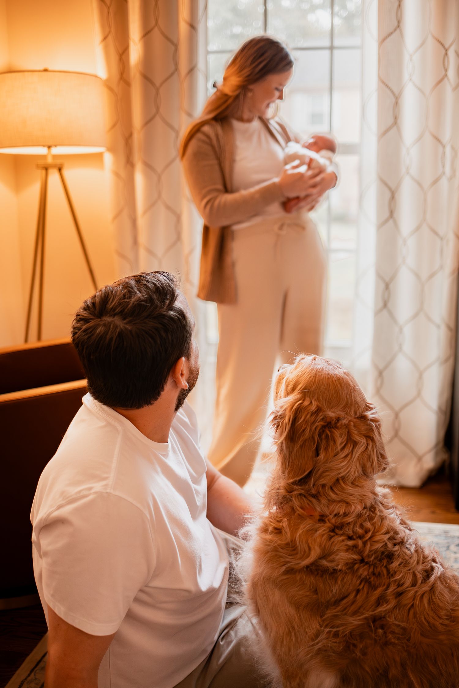 A couple relaxes on a bed in warm lighting with their golden retriever dog beside them.