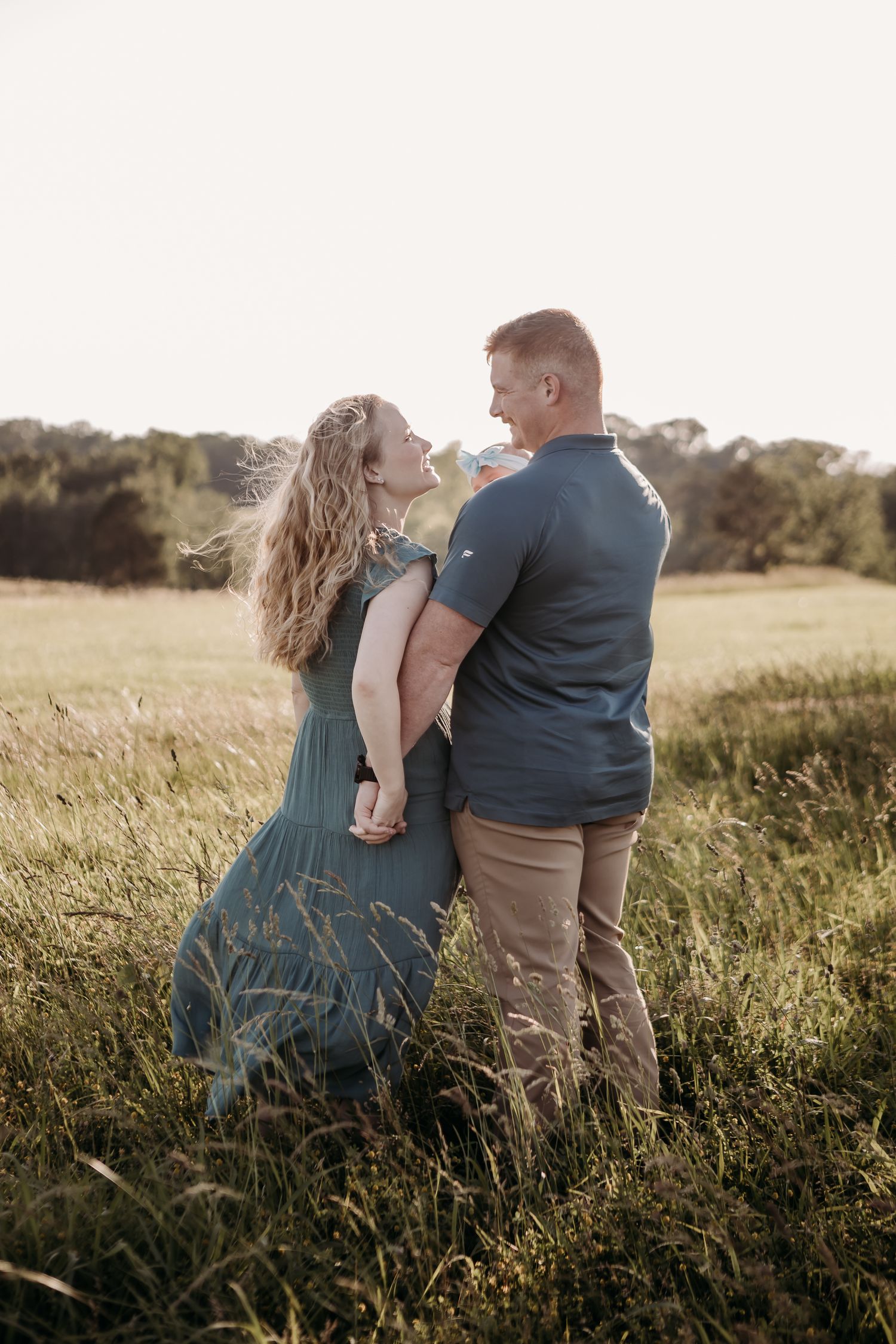 Candid outdoor photo session showing a couple sitting together in a golden grassy field at sunset.