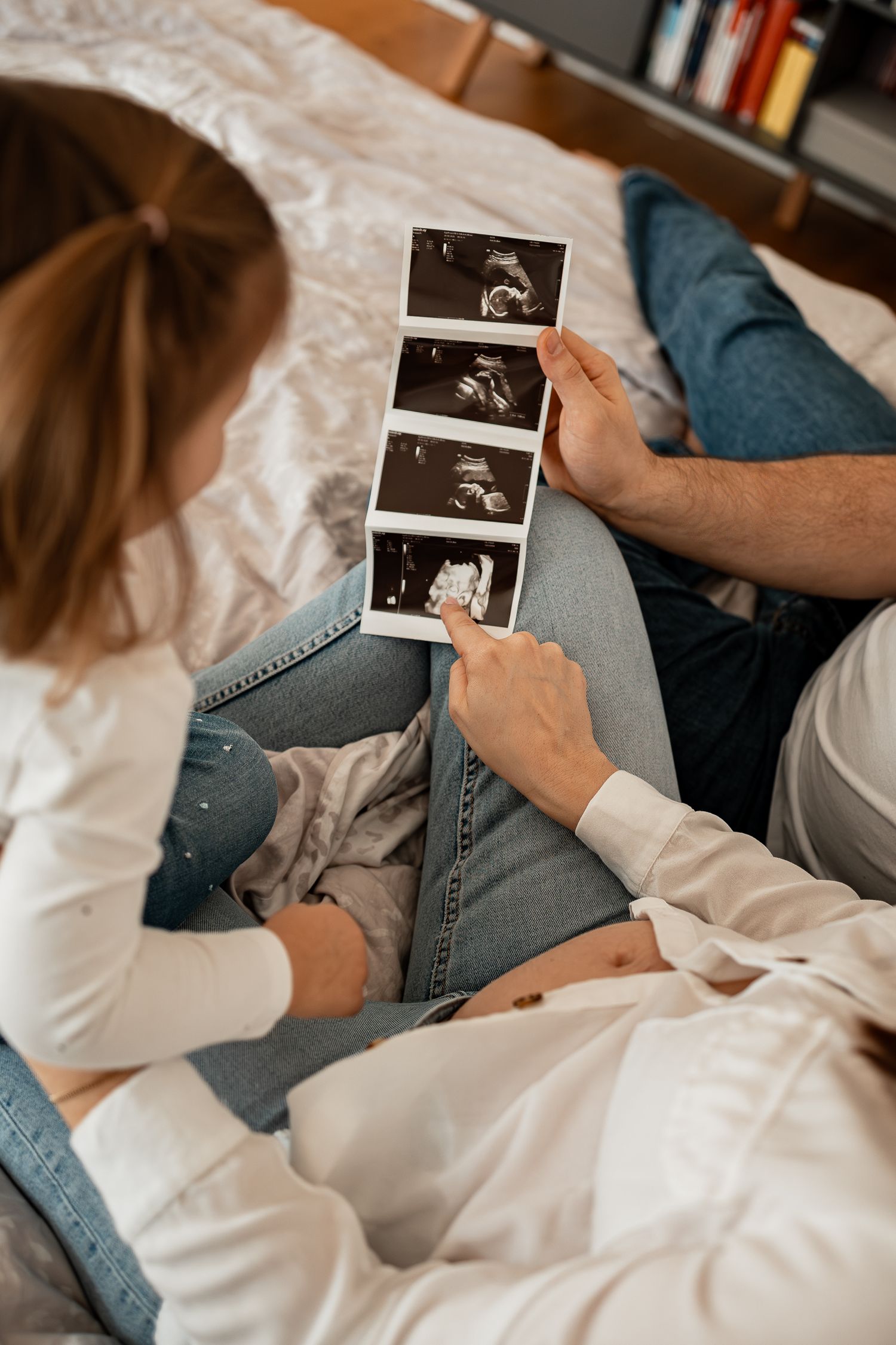 A couple sitting on a bed looking at ultrasound photos together, showing tender moments of pregnancy anticipation.