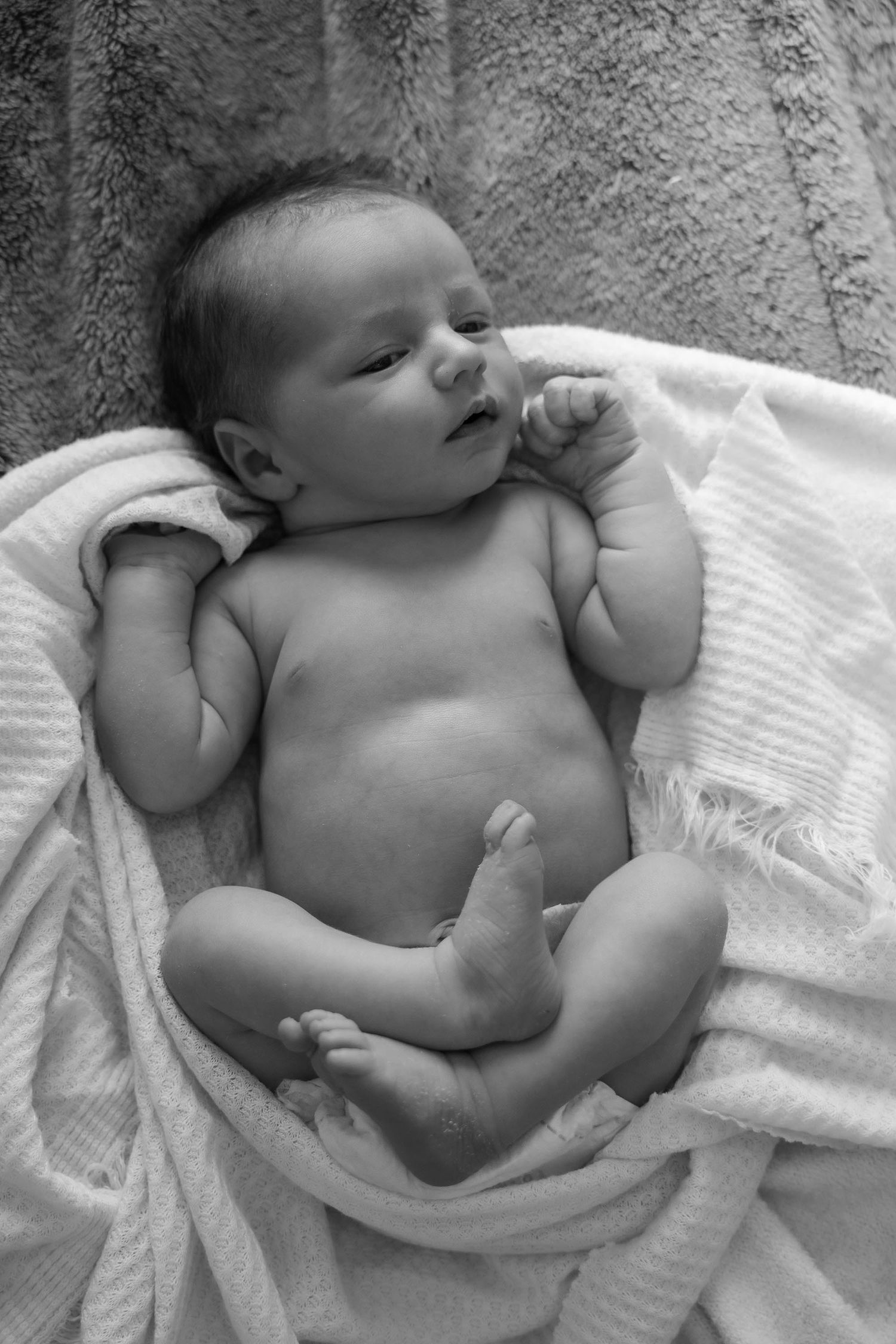 Black and white photo of a newborn baby lying on soft white blankets, arms and legs stretched out.