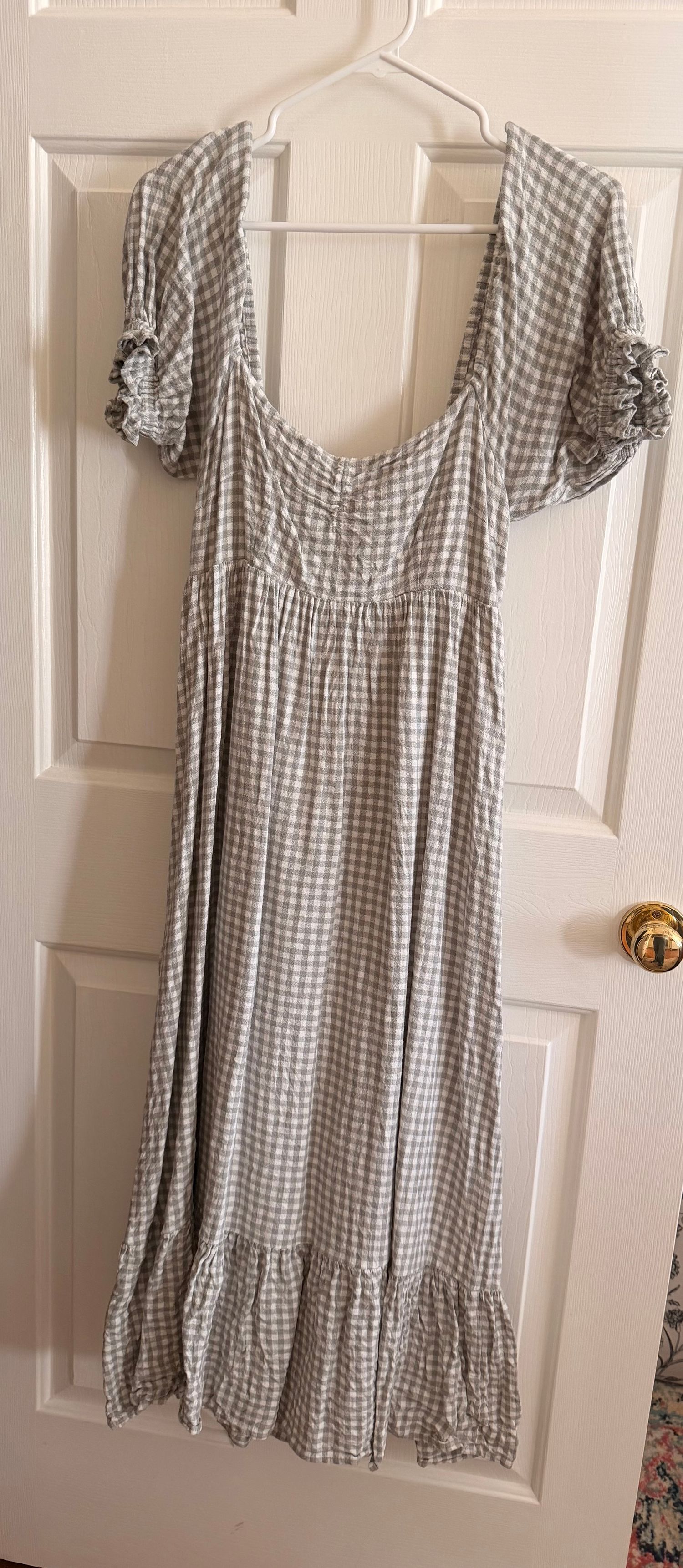 Gray and white gingham check midi dress with ruffle sleeves and hem, empire waist, displayed on hanger against white door.