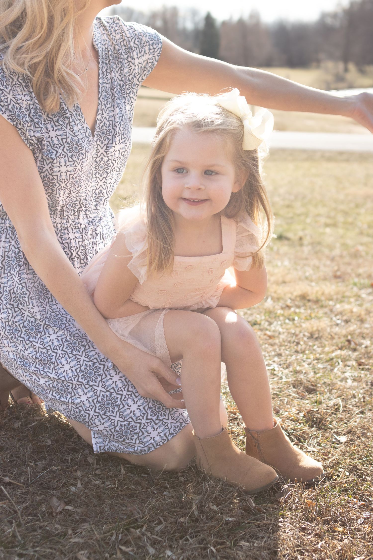 Mother and daughter in sundresses sitting together in sunny field.