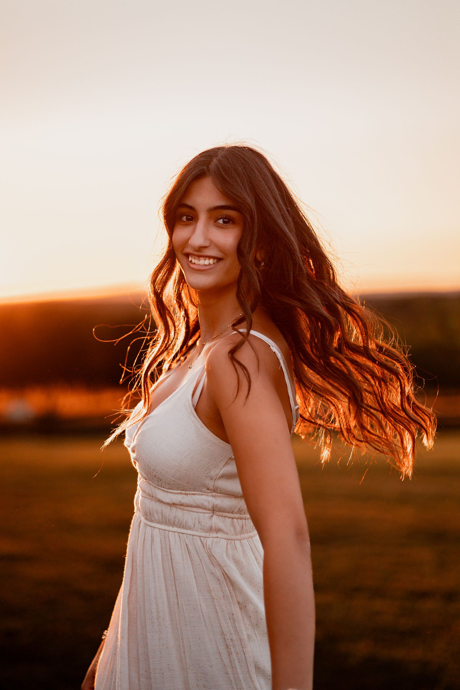 Person in white dress twirls with flowing hair in warm sunset light against a glowing evening sky.