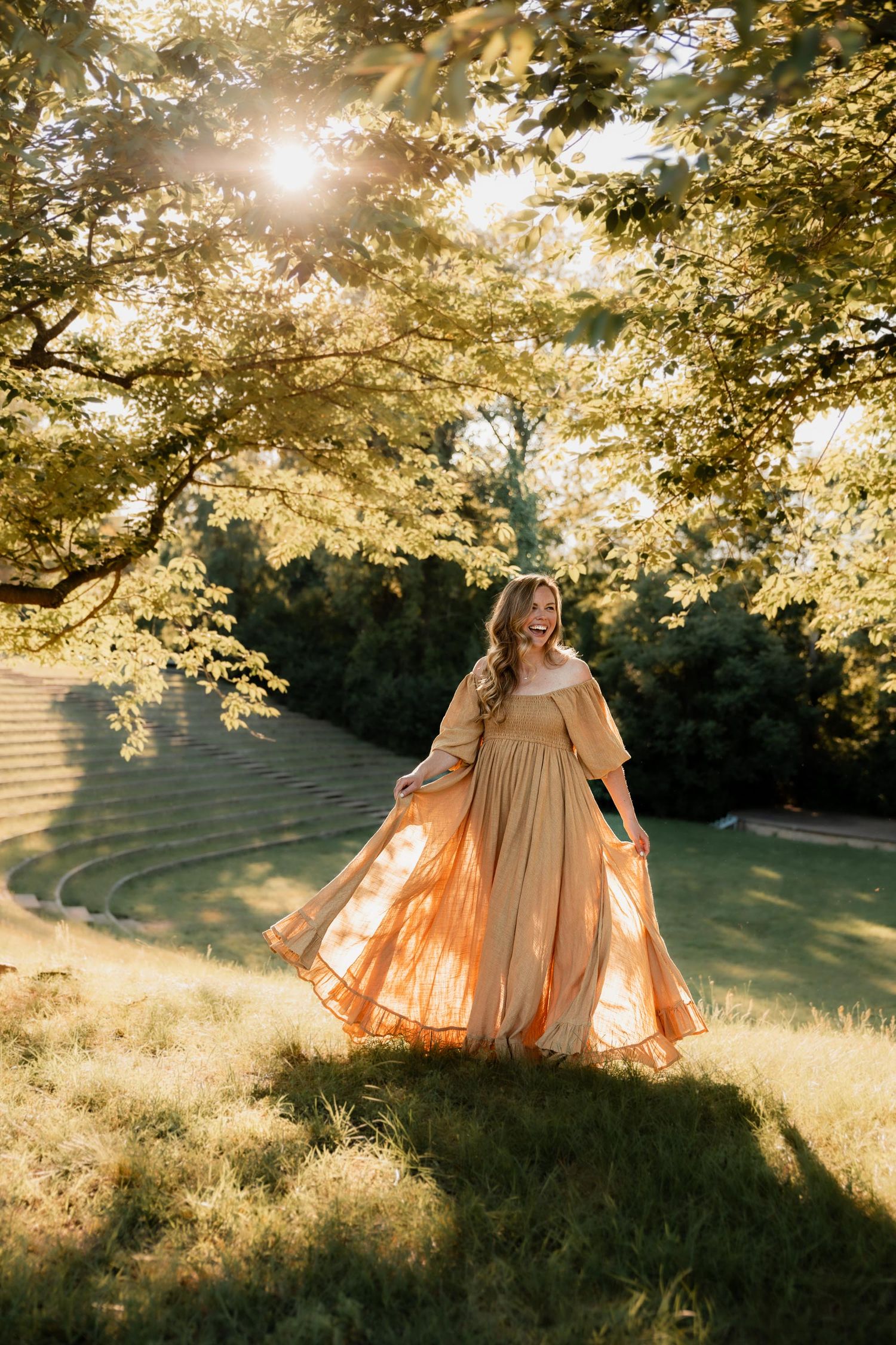 Woman in flowing golden gown twirling under sunlit trees in a lush green park during golden hour.