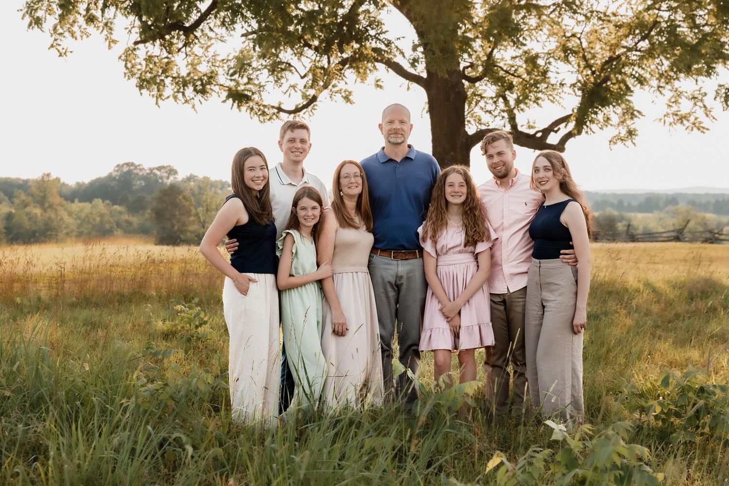 Large family of eight posing outdoors under a oak tree in a golden meadow during sunset for a portrait.