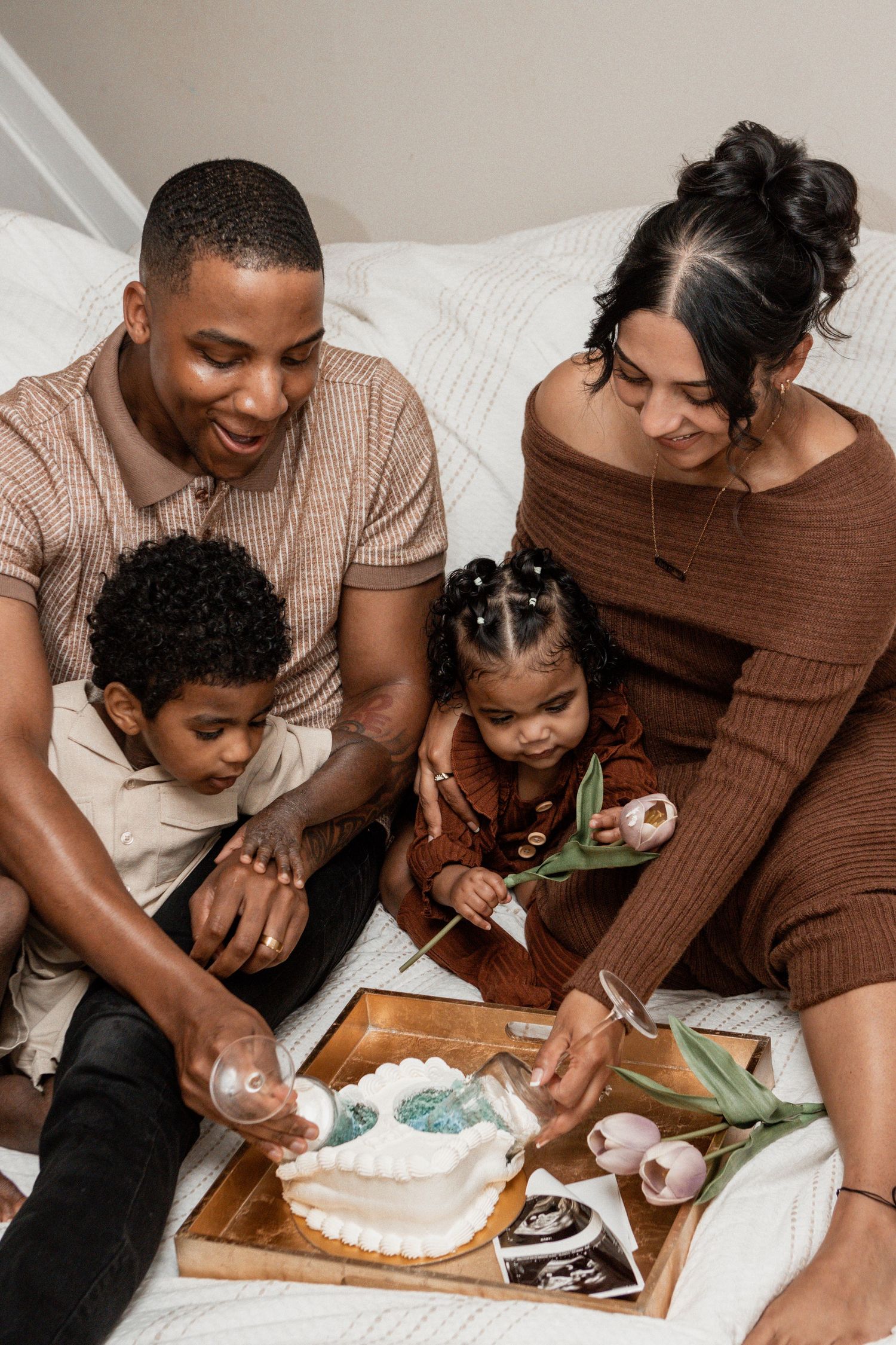 A family gathers around a wooden tray on a bed while enjoying a cozy moment together.