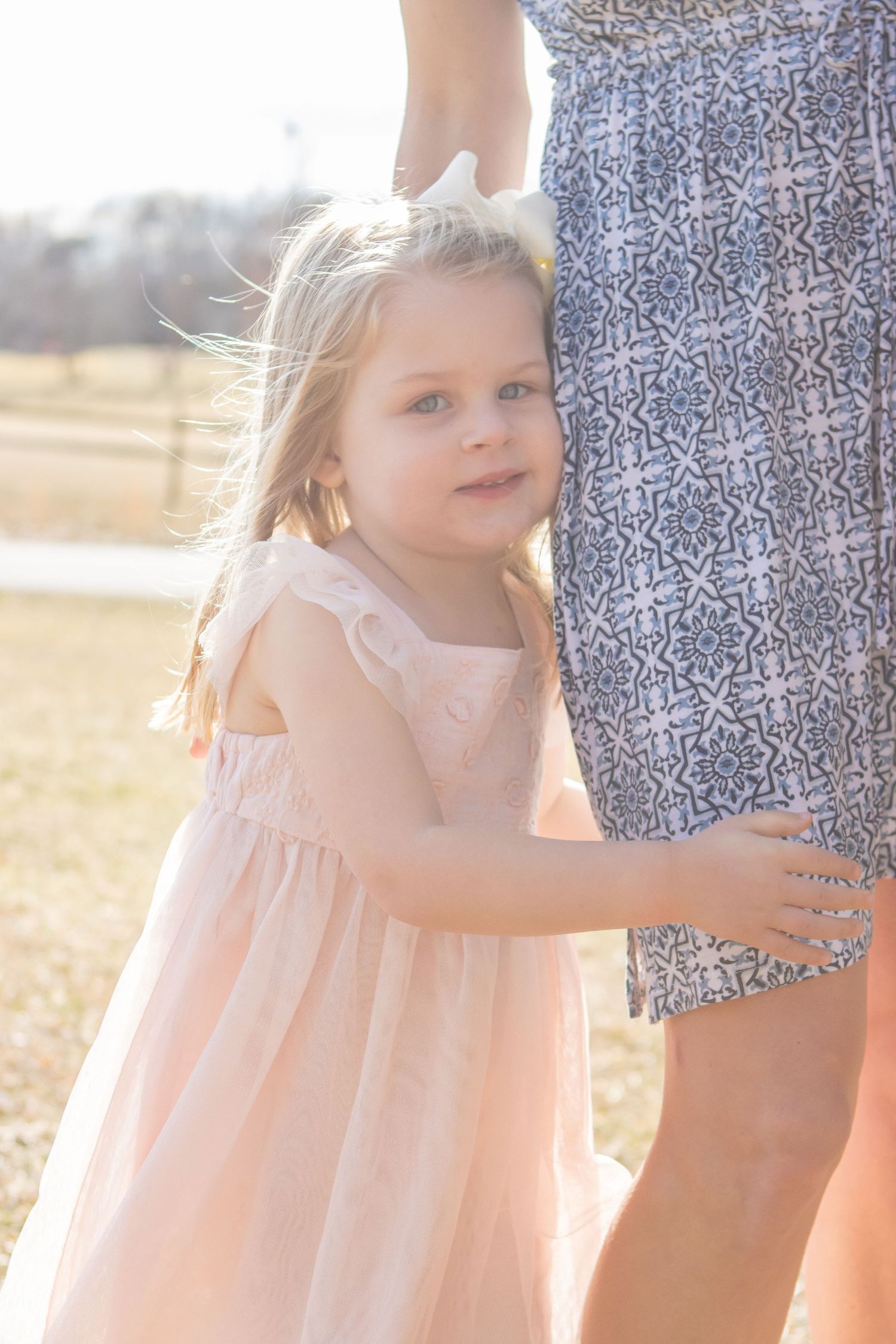 A young child in a pink dress standing close to someone in a patterned dress outdoors.