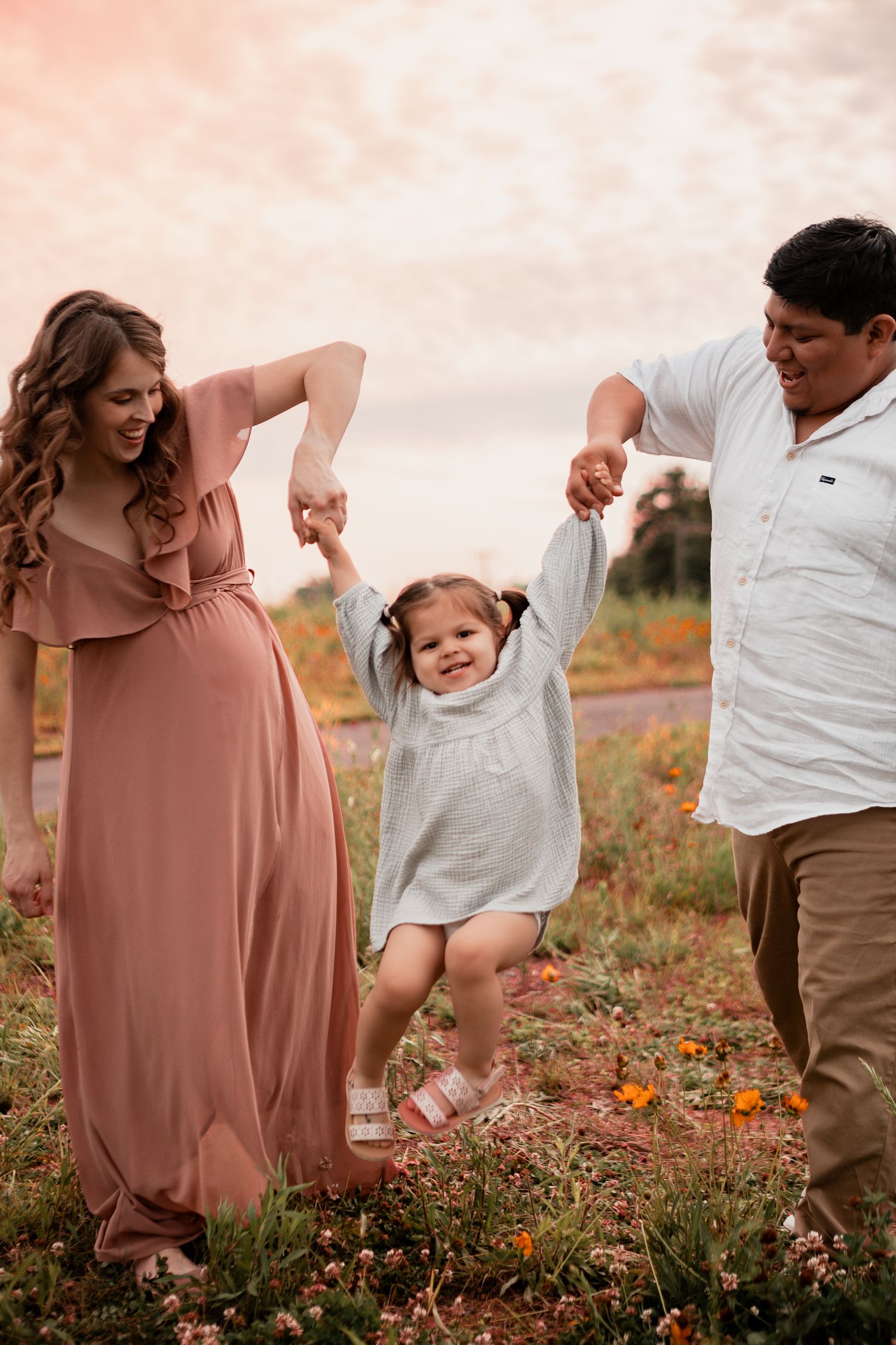 A family plays together in a wildflower field at sunset while wearing casual attire.