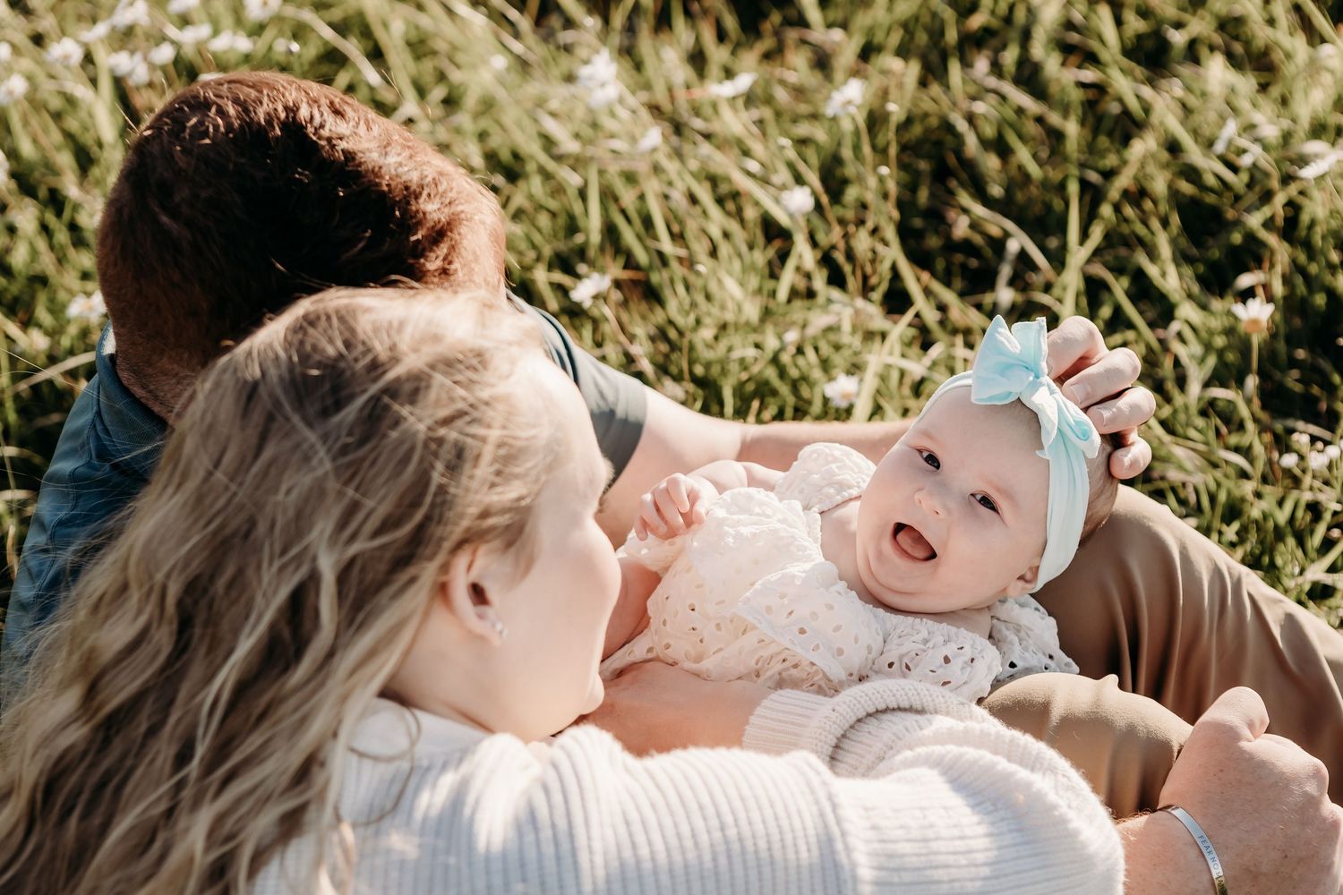 A family lying together on a blanket in tall grass during a sunny afternoon.