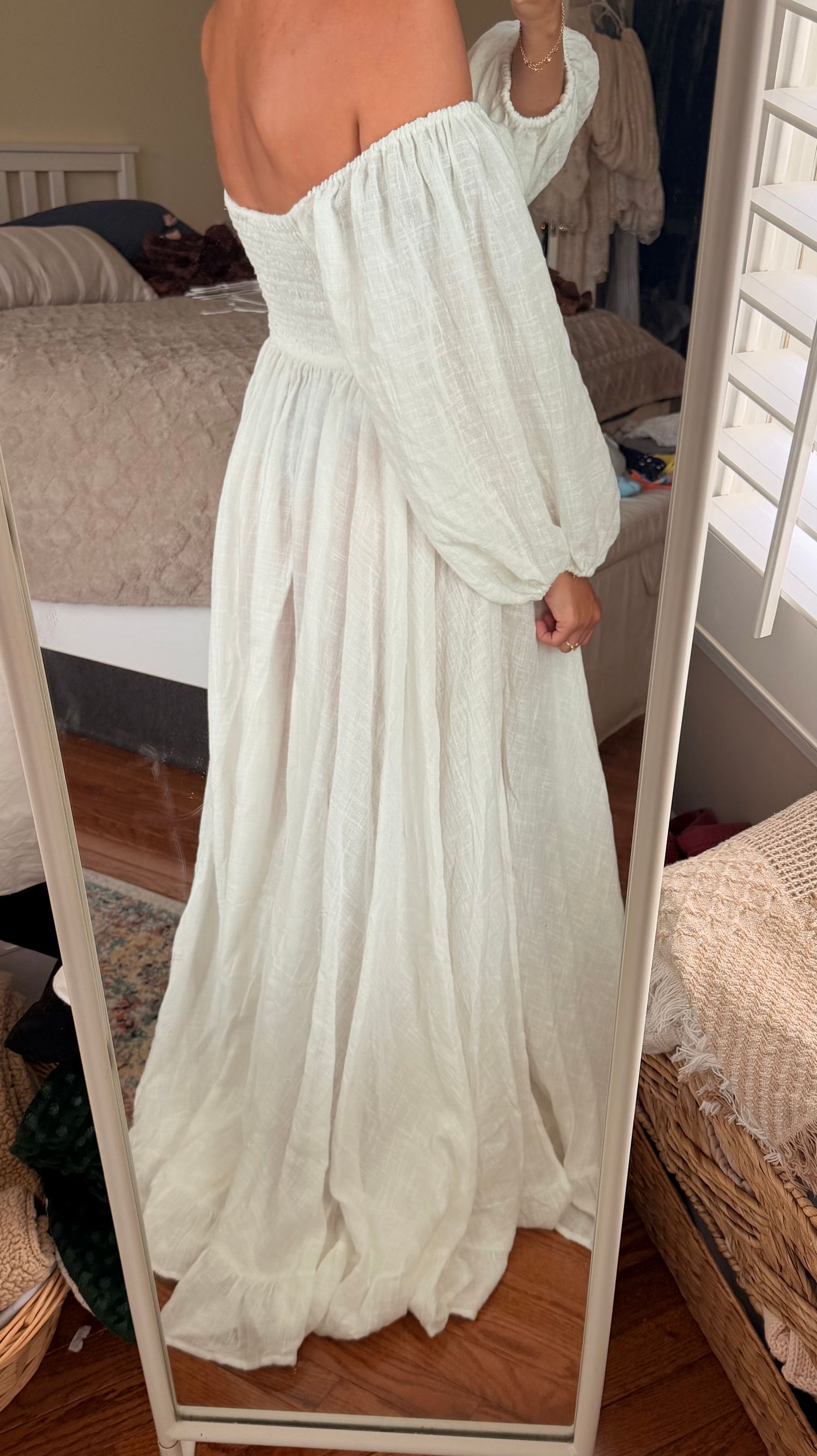 Woman wearing a flowing white off-shoulder maxi dress with billowy long sleeves, photographed in mirror reflection.