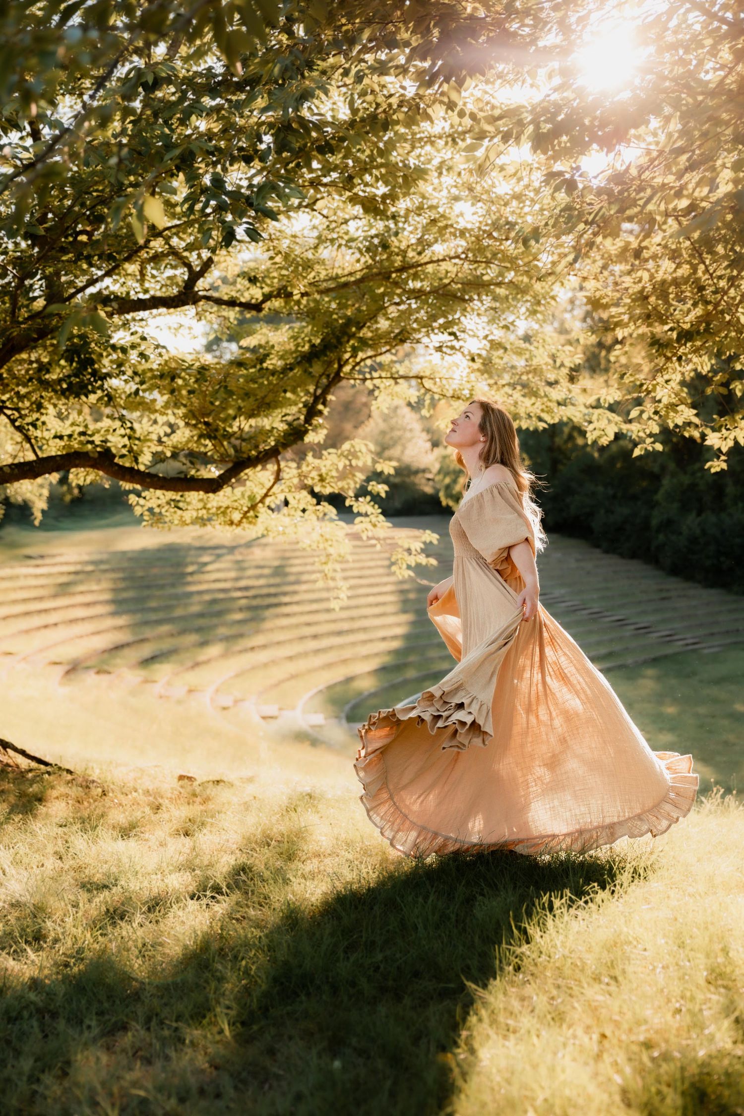Woman in flowing peach gown twirling under sunlit trees in a lush green garden at golden hour.