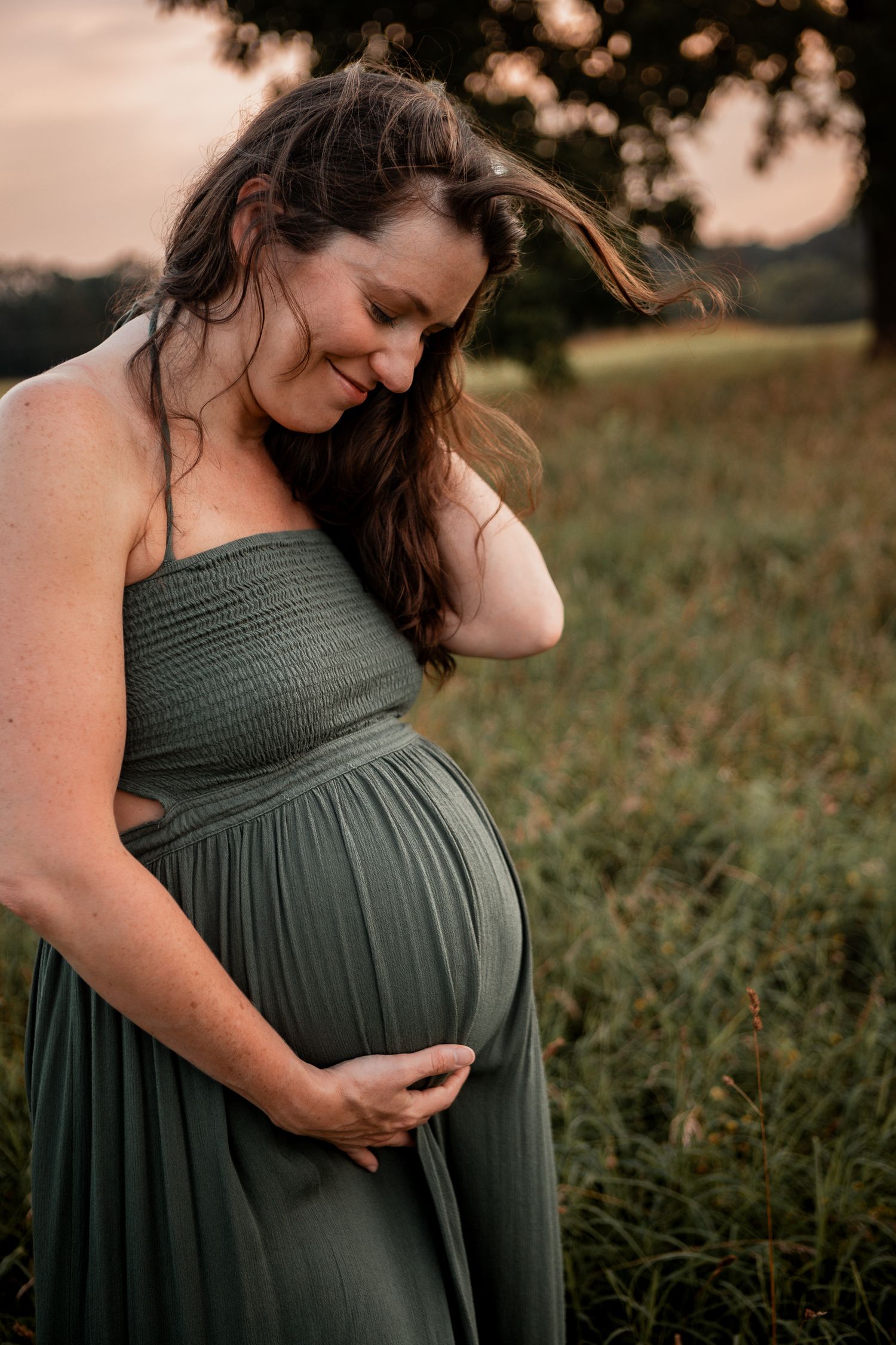 A maternity photoshoot in a green dress shows tender moments against a golden sunset in a grassy field.