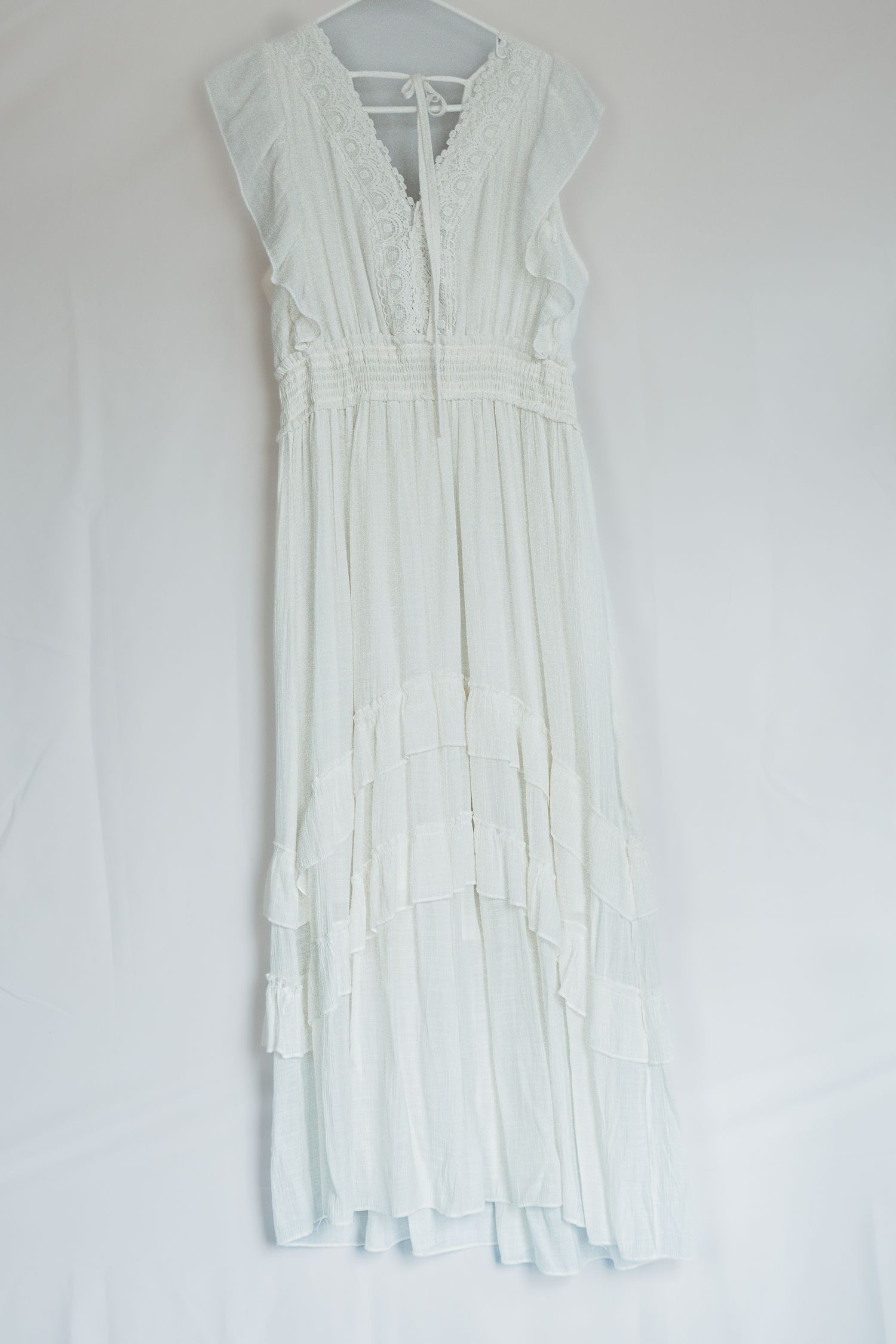 White empire waist sundress with lace details and cap sleeves hangs on display against a light wall.