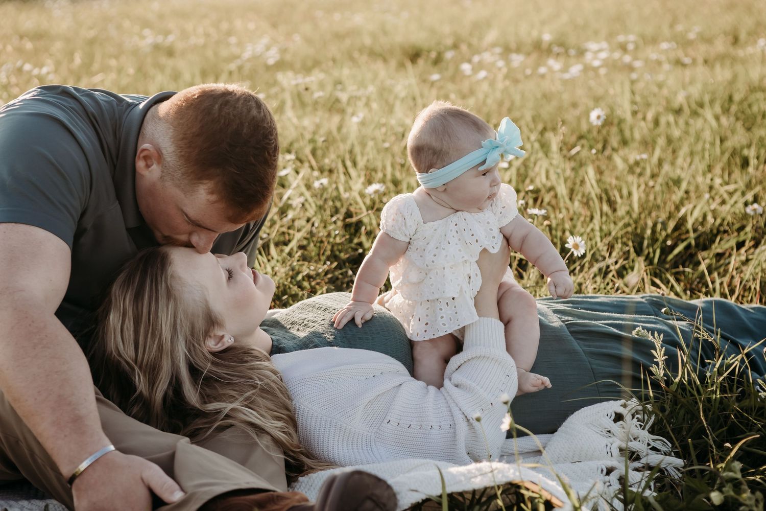 Family having a sunset picnic together on a blanket in a golden wheat field during summer.