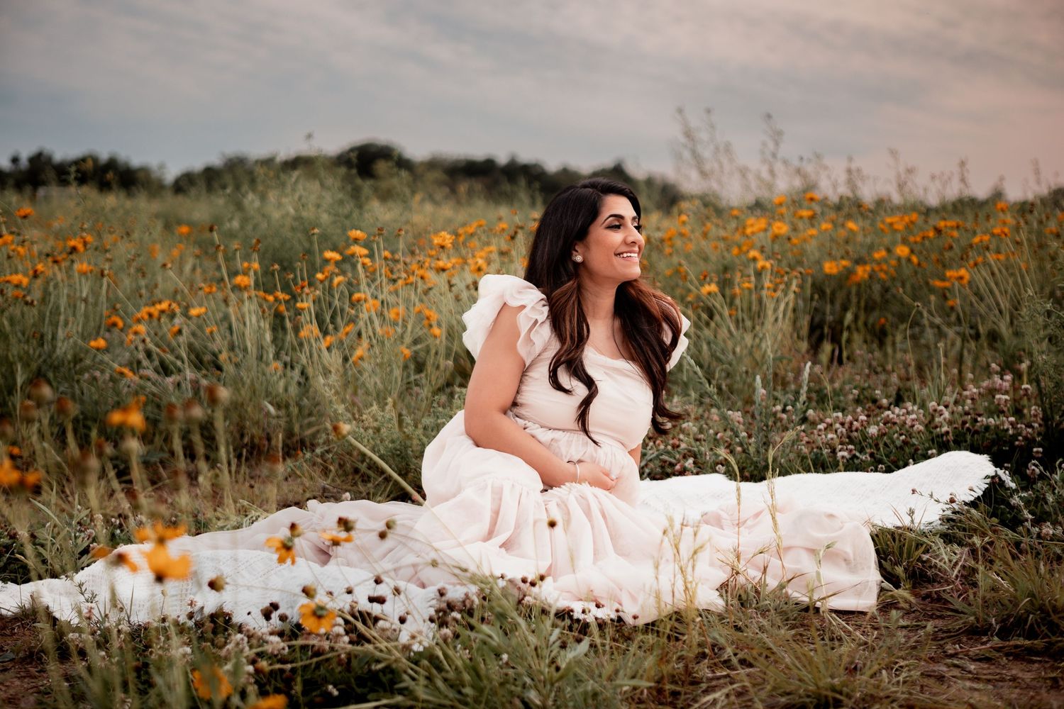A person in a flowing white dress sits gracefully among vibrant orange wildflowers in a meadow during golden hour.