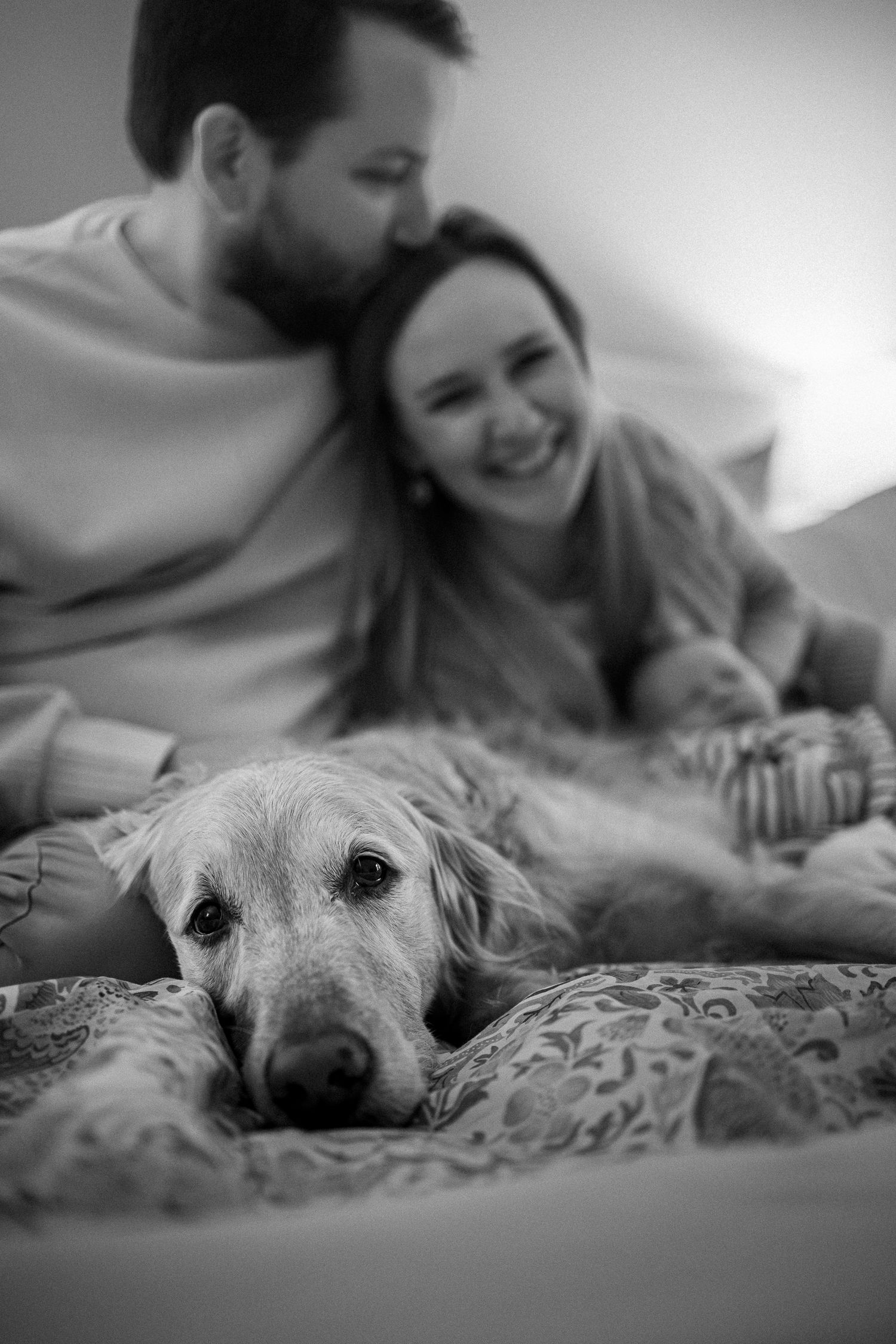 A black and white photo captures intimate family moments with their golden retriever on the bed.