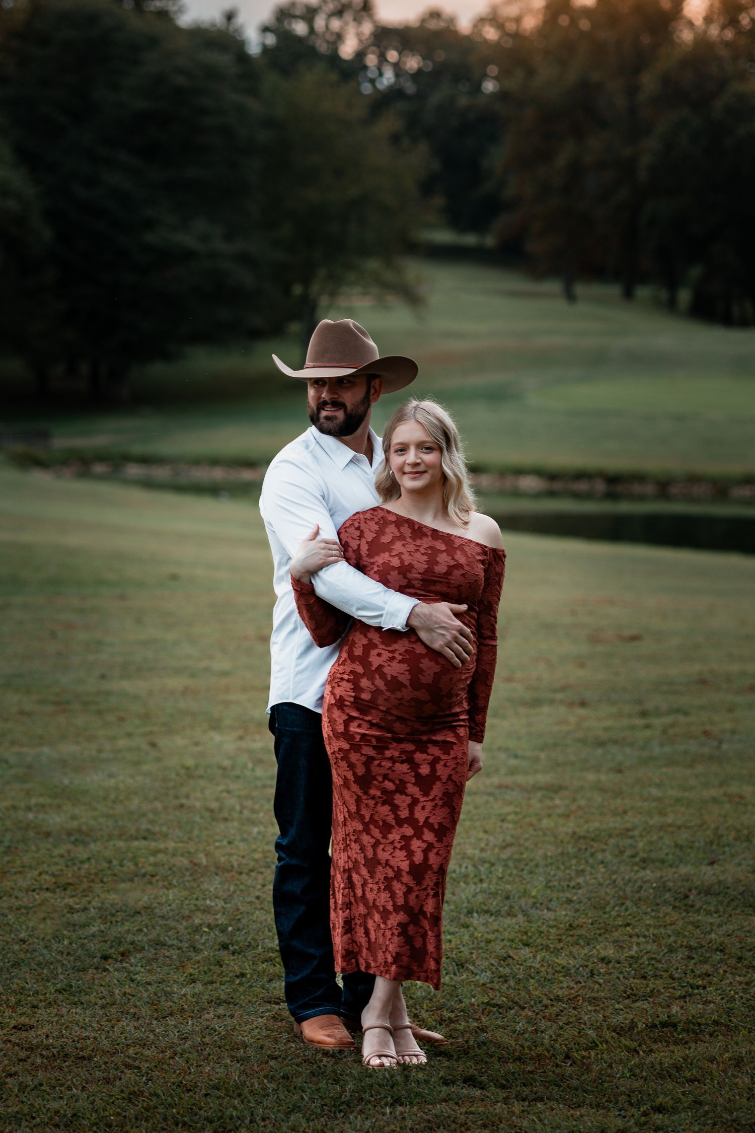 Sunset maternity photography session showing couple embracing in a rustic outdoor setting.