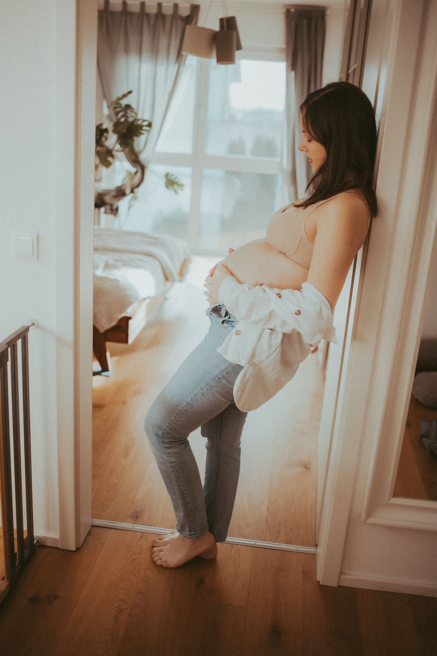 Multiple shots of an expectant mother in white top and jeans posing near a window in natural light.