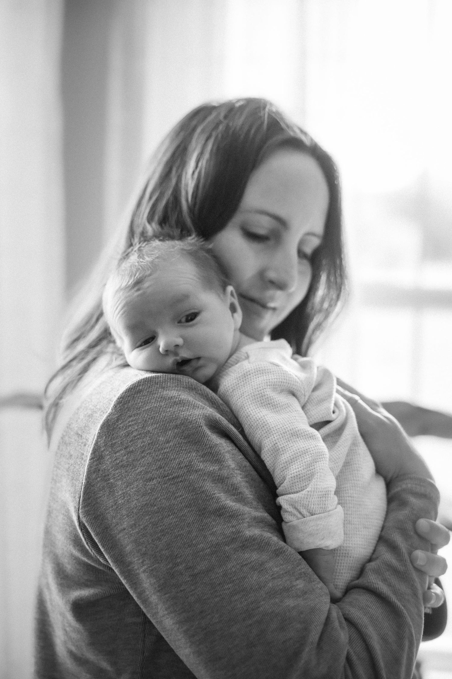 Black and white photo of a mother tenderly holding her newborn baby close to her chest.
