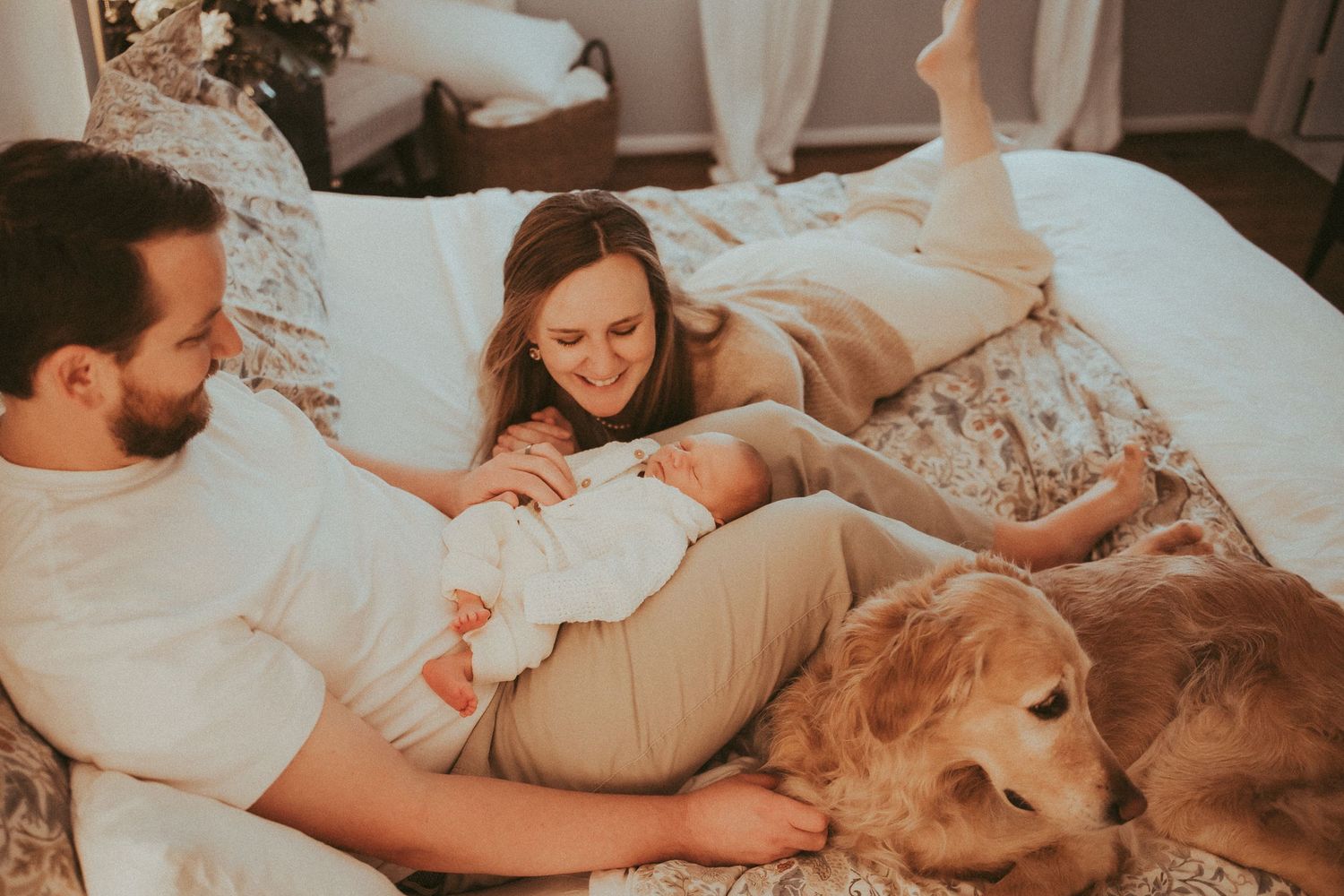 A couple relaxes in bed with their golden retriever dog during a cozy lifestyle photoshoot.