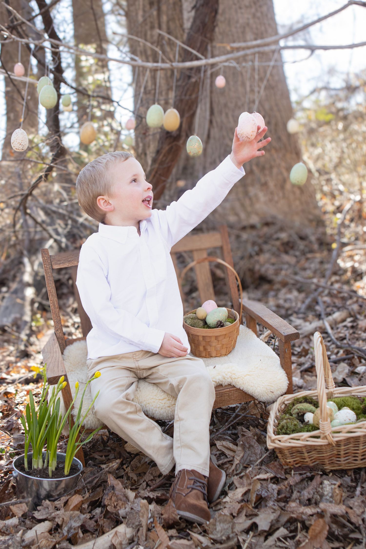 A springtime scene shows a child reaching for decorated Easter eggs hanging from tree branches.