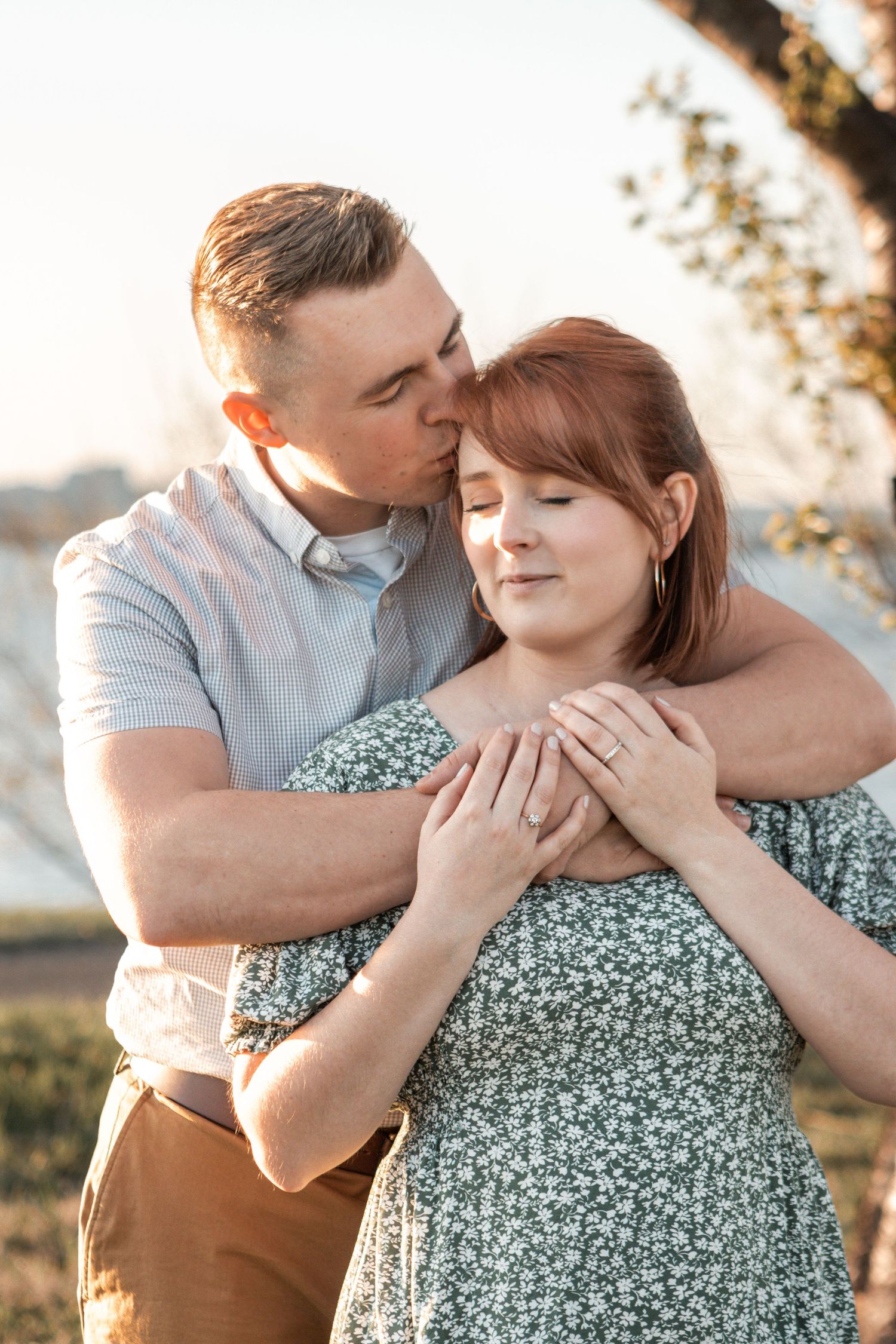 A couple shares an intimate embrace in a floral dress and casual wear during golden hour outdoors.