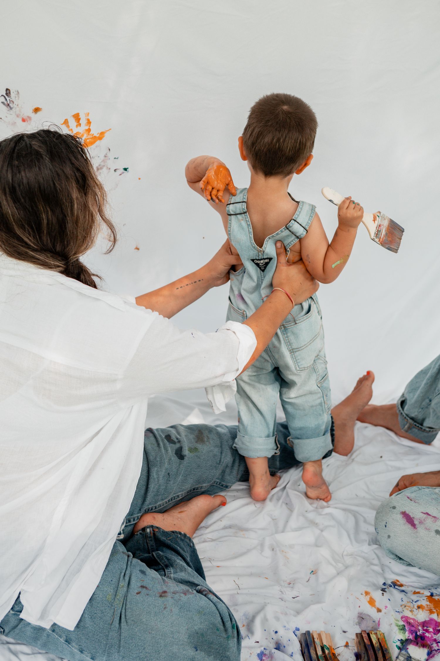 Paint splattered family having messy creative fun while sitting on white fabric together.