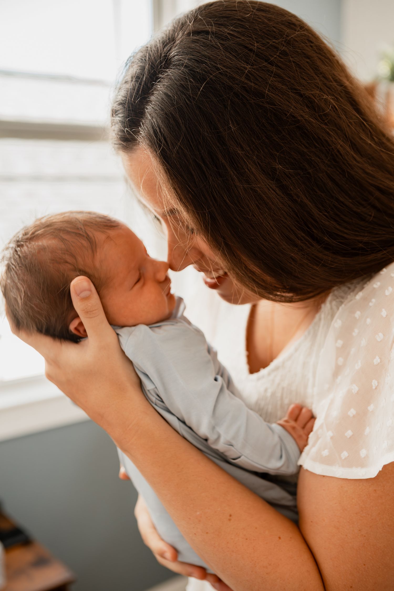 A gentle moment of bonding between parent and newborn in front of a window.