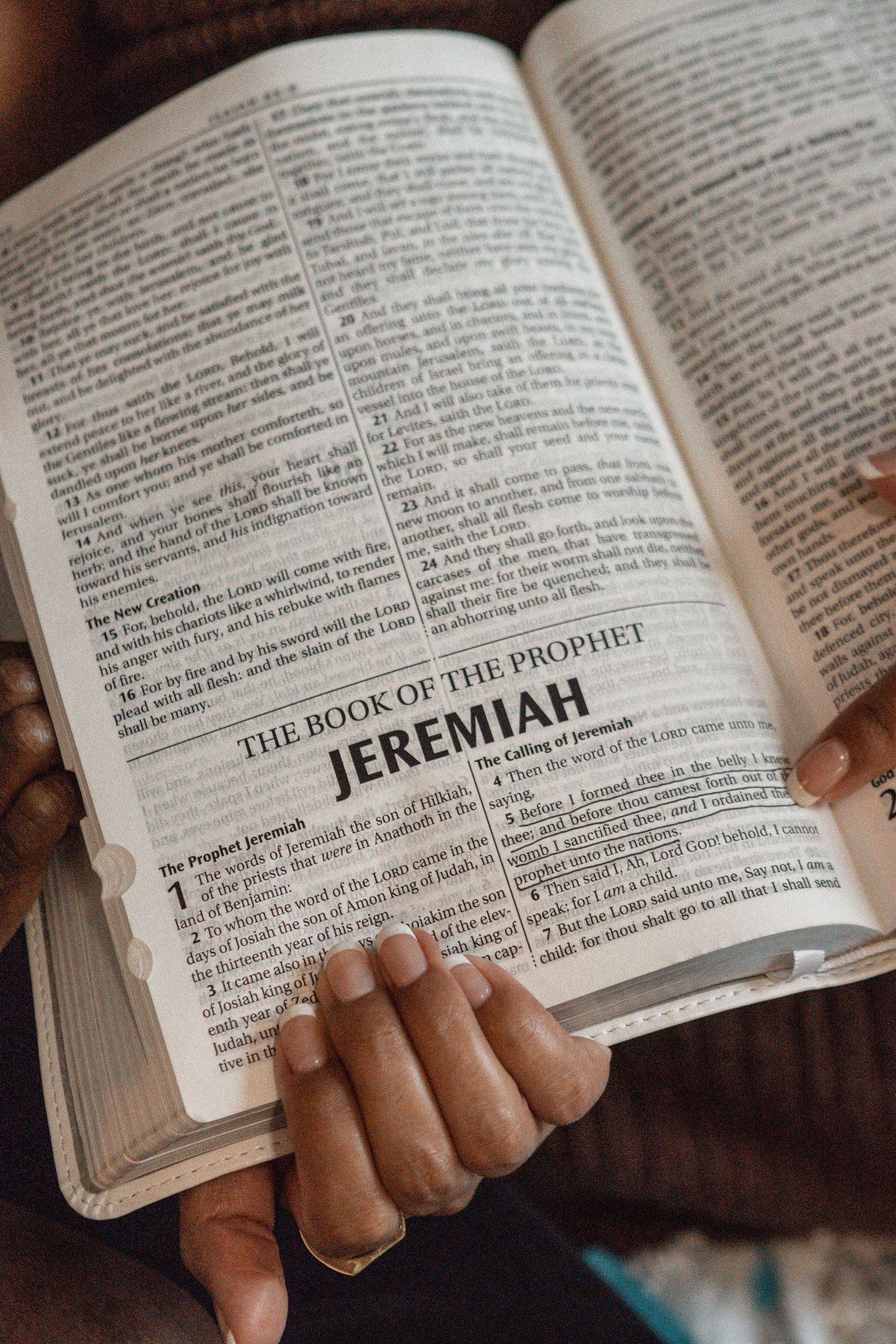 An open Bible showing the Book of Jeremiah title page with hands holding the pages.