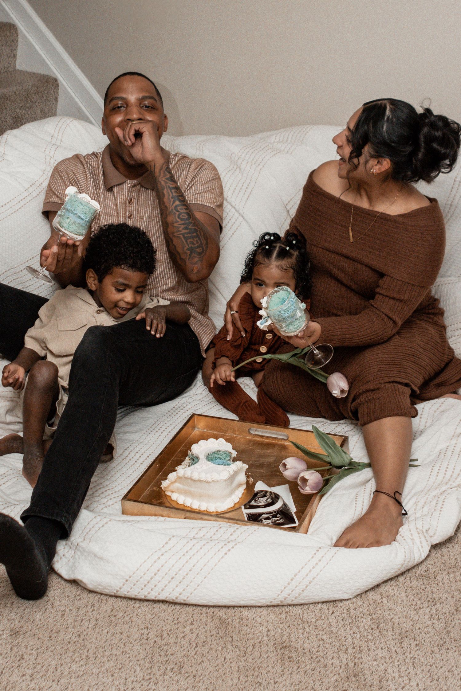 Family enjoying hot beverages and treats together on a cozy white couch with a wooden serving tray.