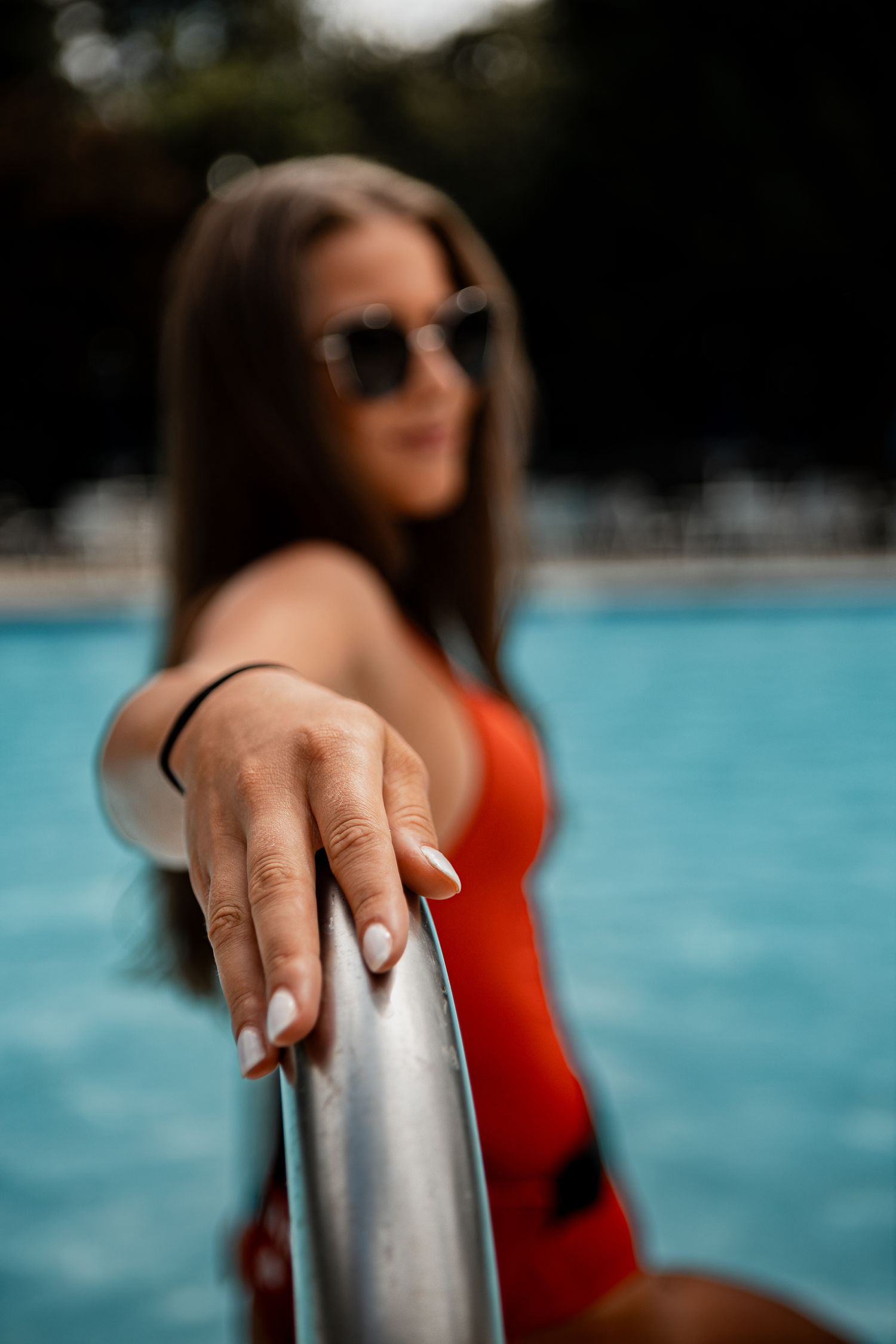 Close up of hand touching metal pool railing with turquoise water in background.