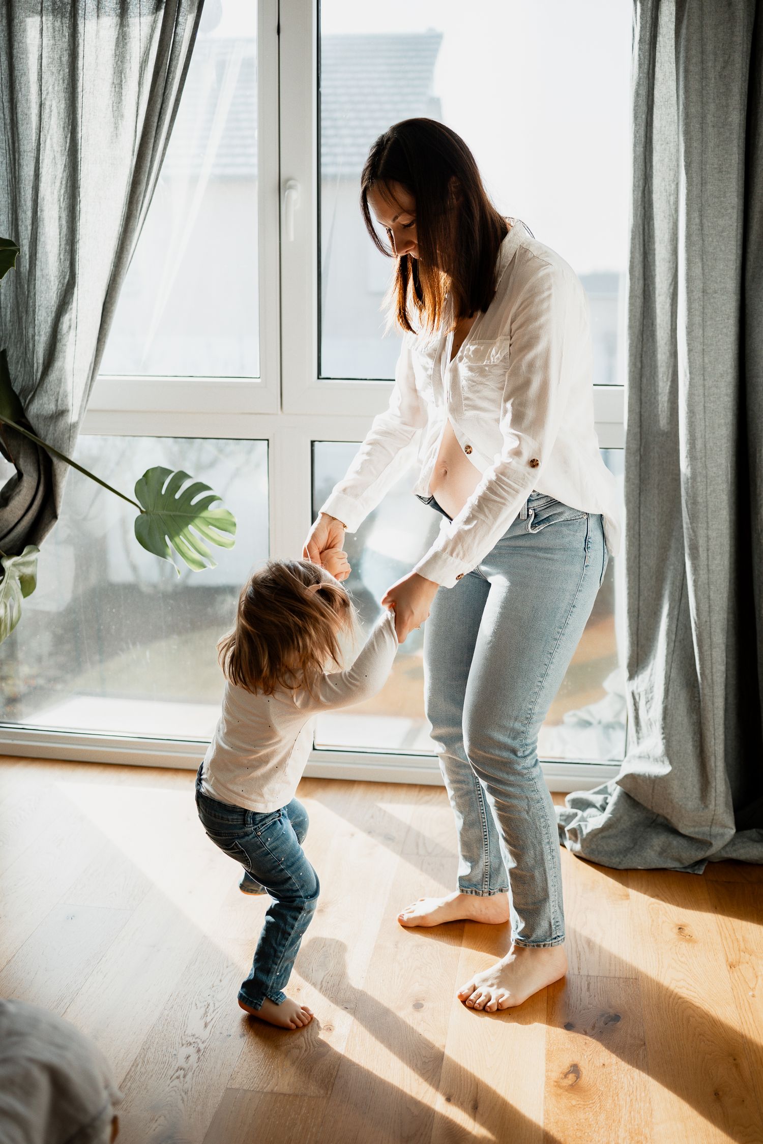 Parent and child playing together in a sunlit living room with curtains and hardwood floors.