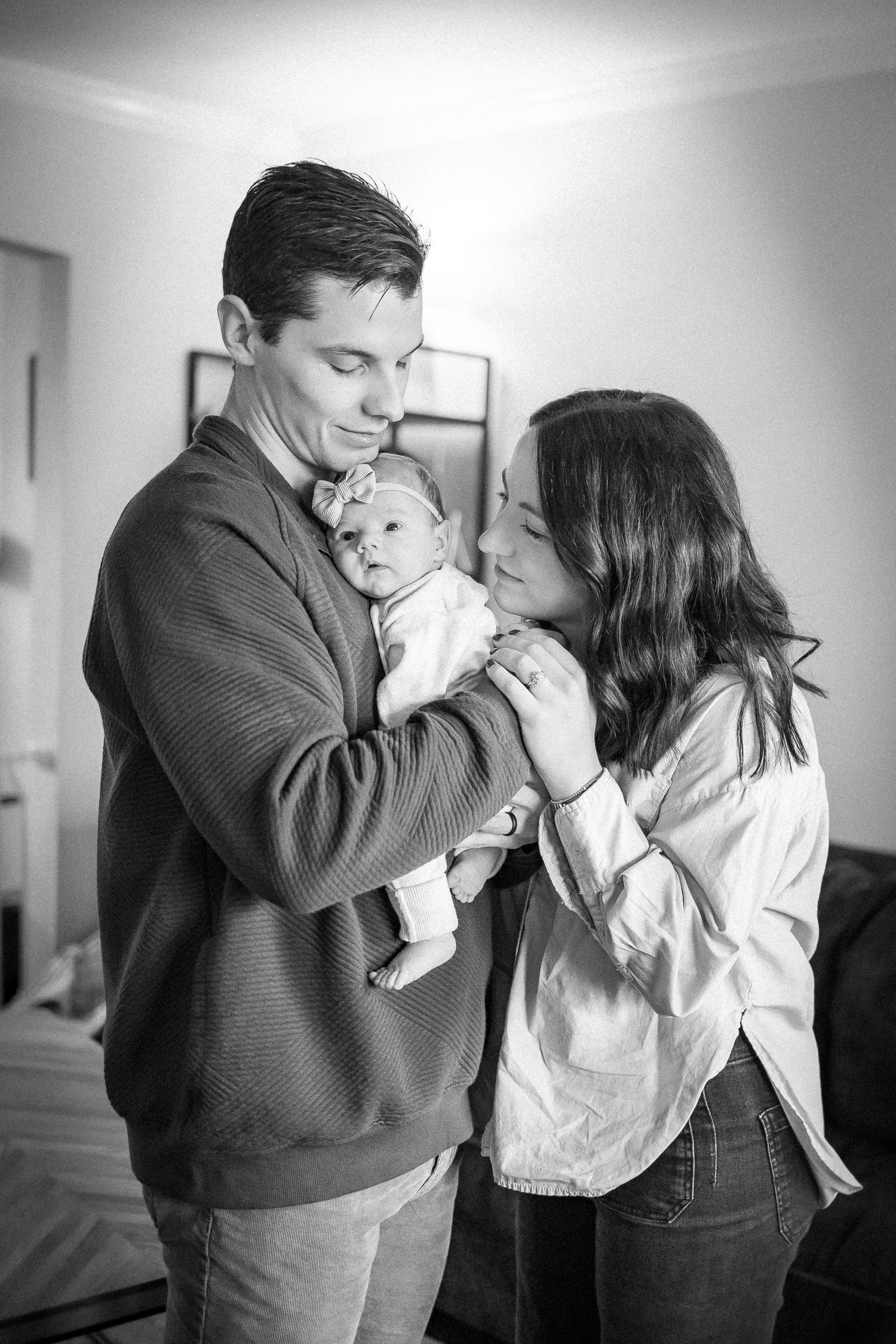 A black and white photo series shows tender moments between a couple and their baby in an intimate setting.