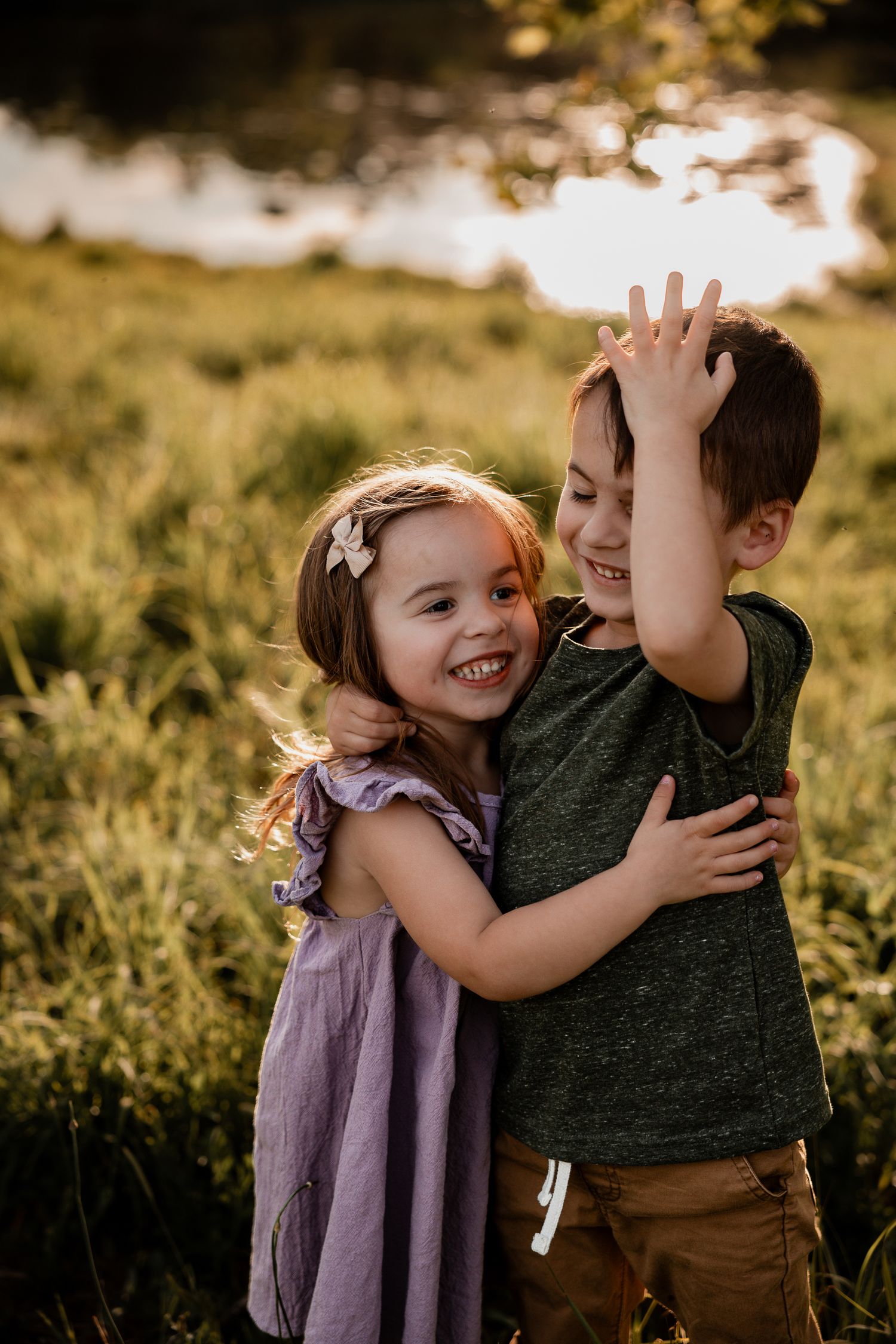 Two happy children hugging in a sunlit meadow, a girl in purple dress and boy in green shirt sharing a joyful embrace.