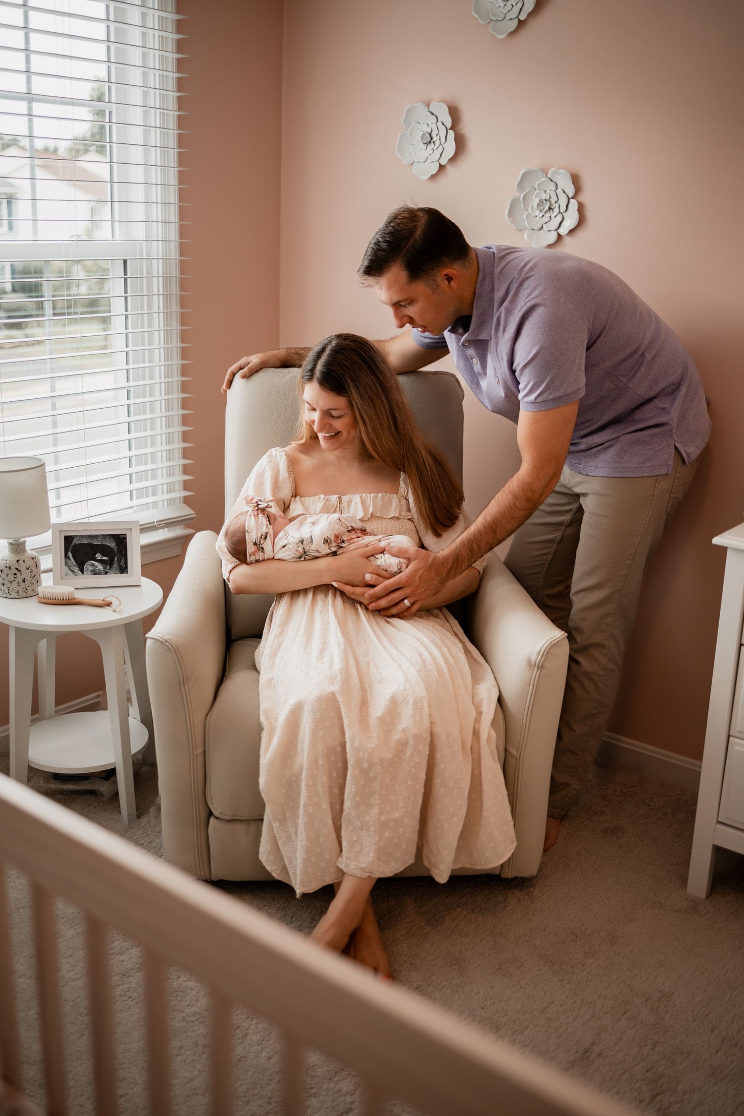 Expectant couple sharing an intimate moment in a nursery with pink walls and white floral decor.