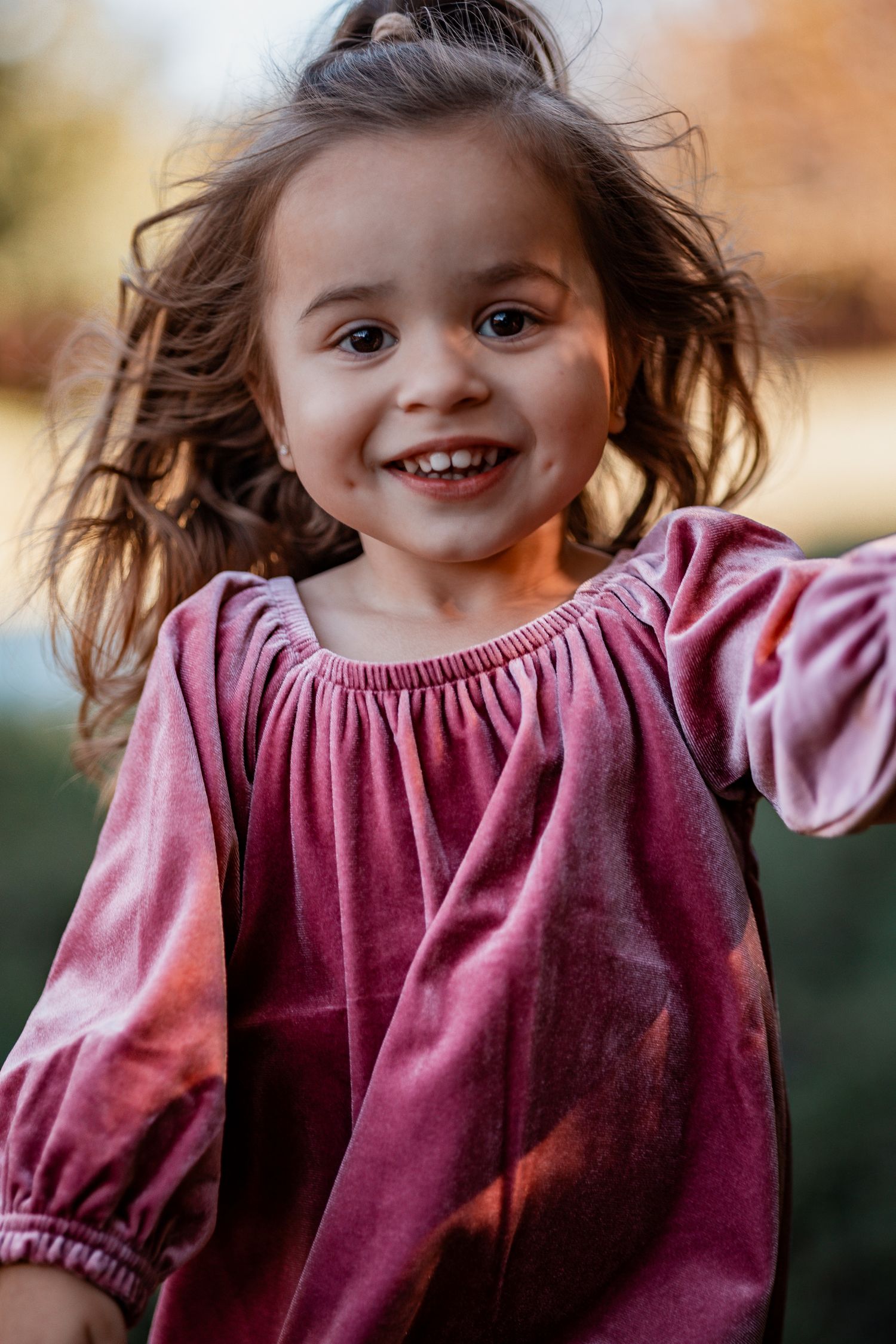 A series of five candid photos showing a child in a burgundy dress with windblown hair expressing joyful emotions.