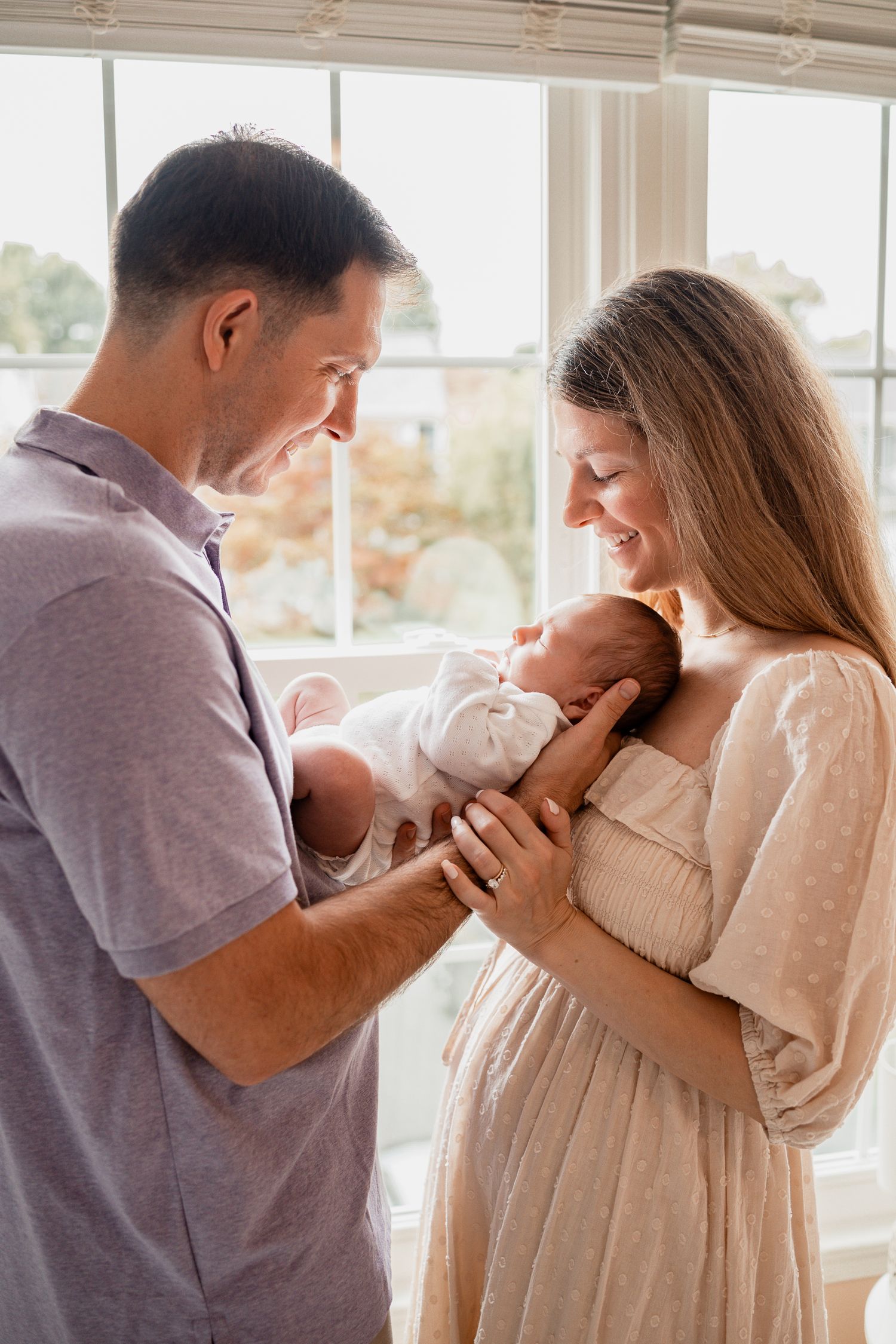 A series of four tender moments between a couple and their newborn baby shown in a bright window-lit setting.