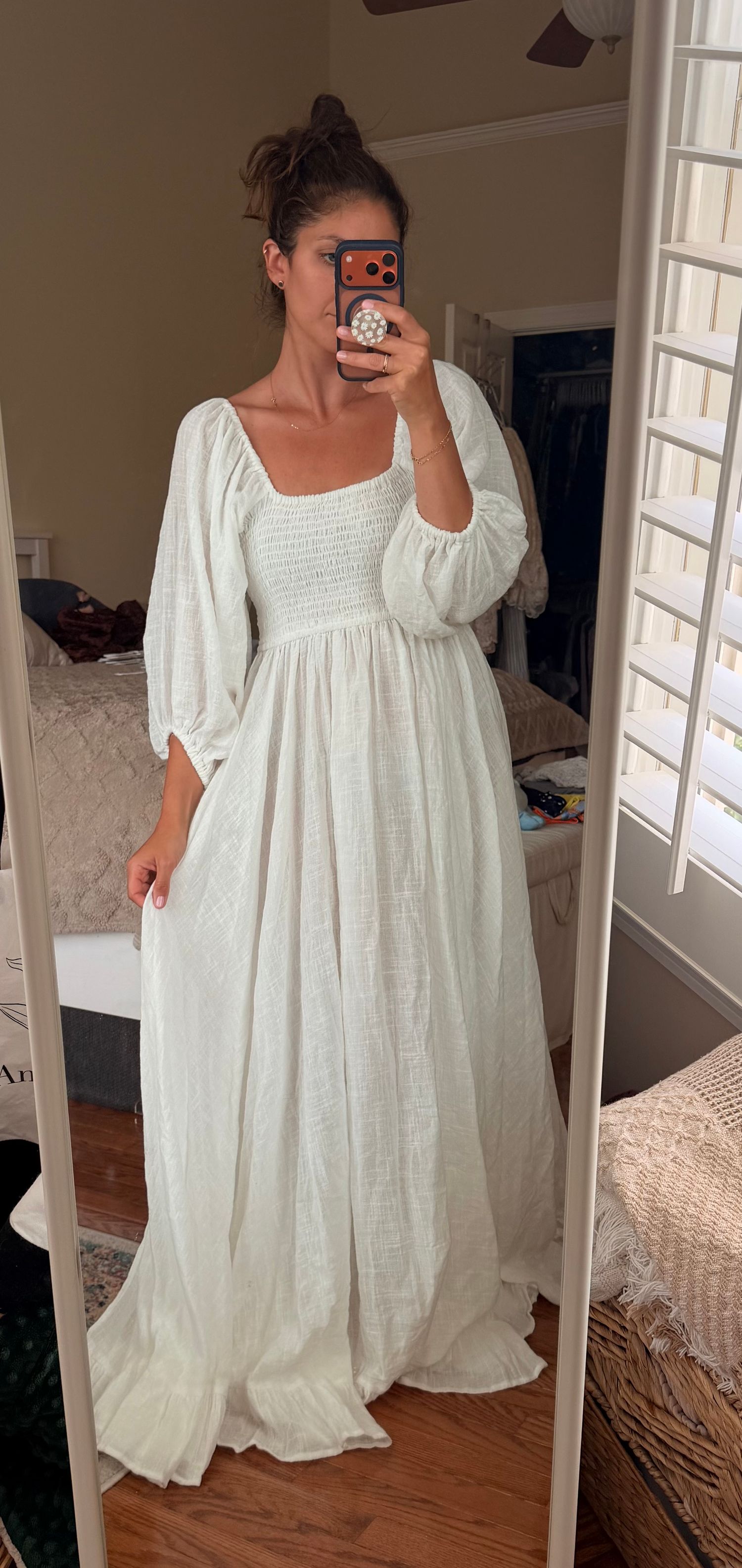 Woman in white maxi dress with smocked bodice and puff sleeves takes mirror selfie in bedroom.