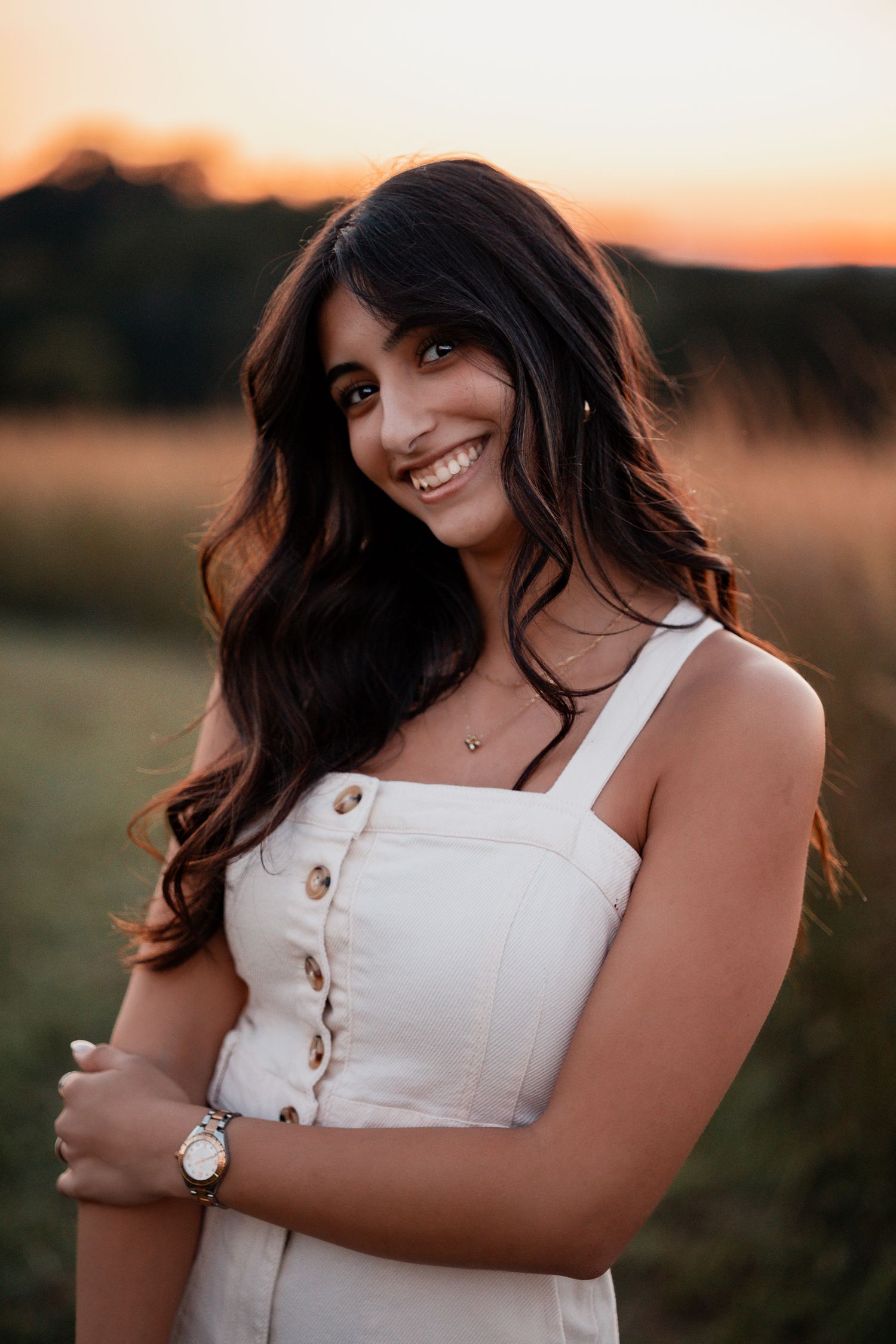 Sunset photoshoot showing a person in a white button-up dress against a warm glowing sky.