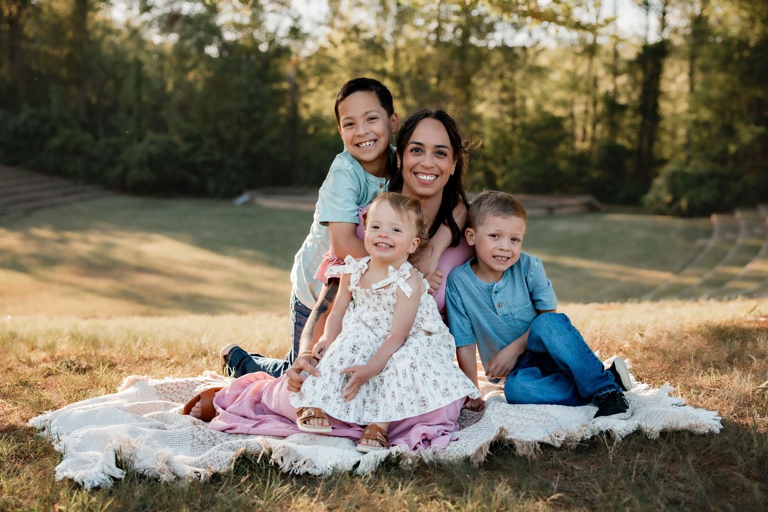 Happy family of four sitting on a blanket in a sunny outdoor field, smiling together.