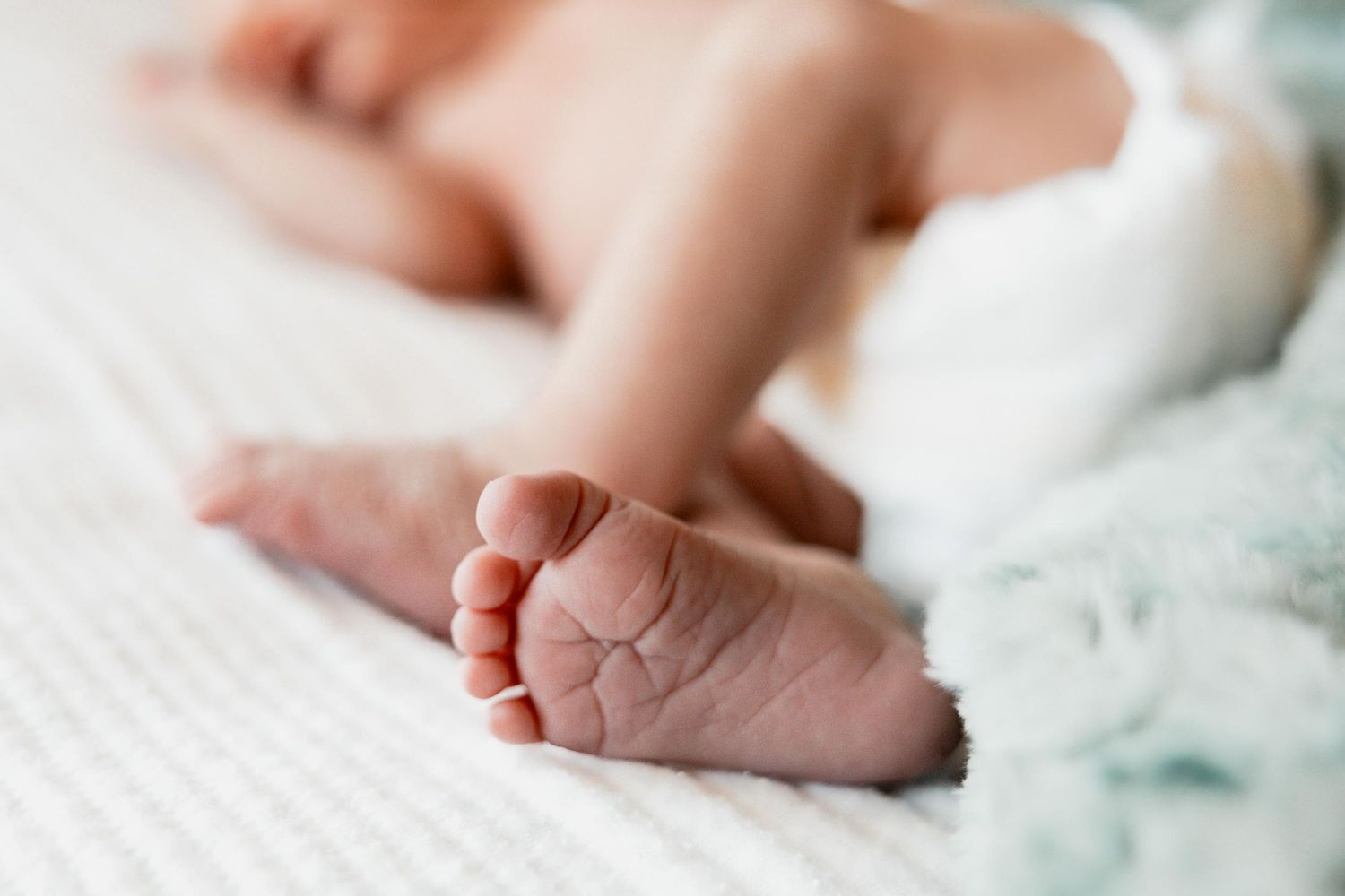Close-up of tiny newborn baby feet resting on a soft white blanket with a light blue cloth nearby.