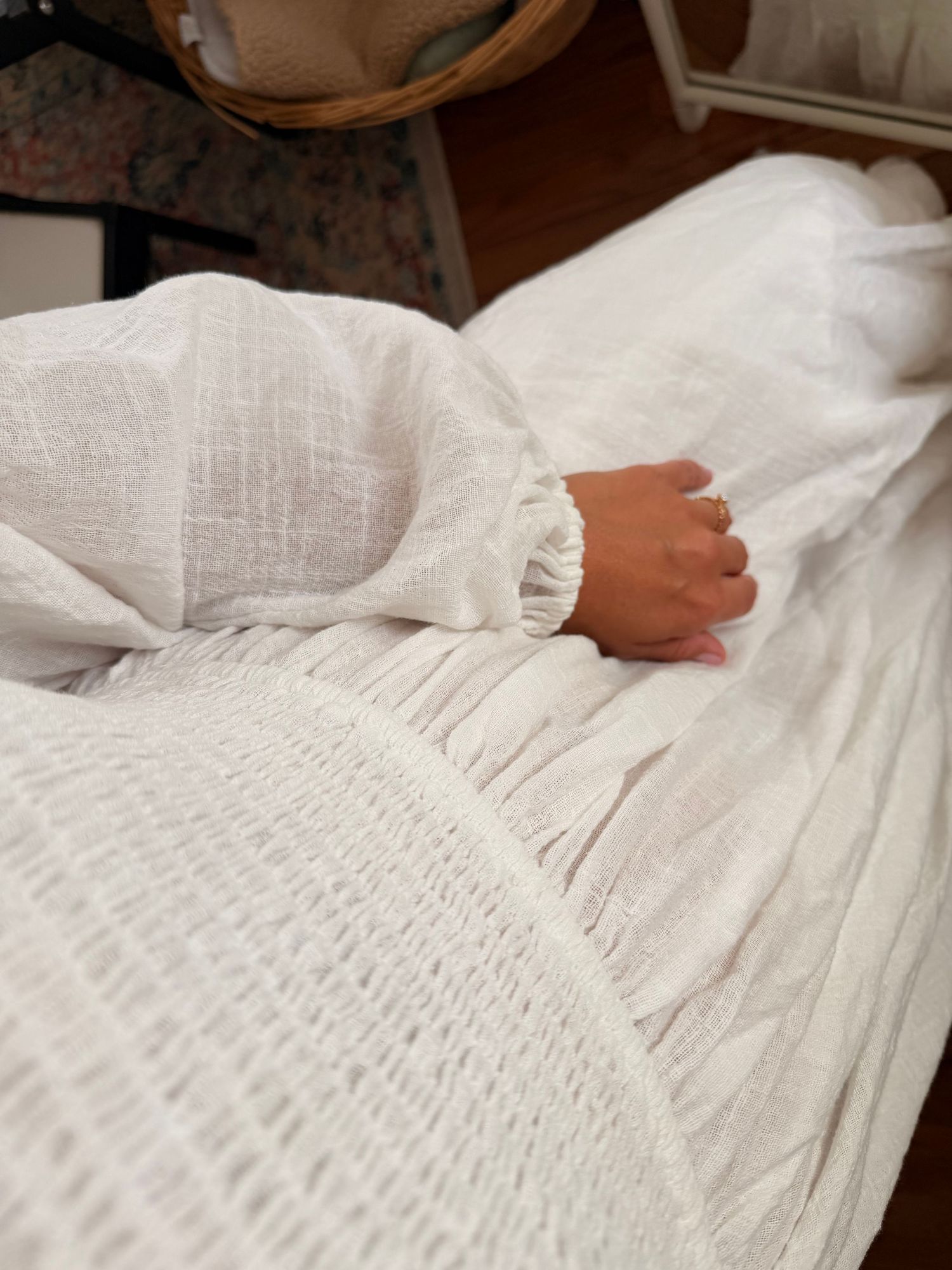 Close-up of a hand resting on white smocked linen bedding with ruffled sleeve detail.