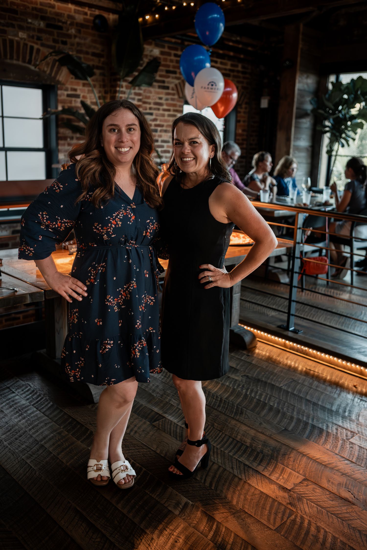Party guests enjoying festivities at a rustic brick venue with dim lighting and blue and red balloons.