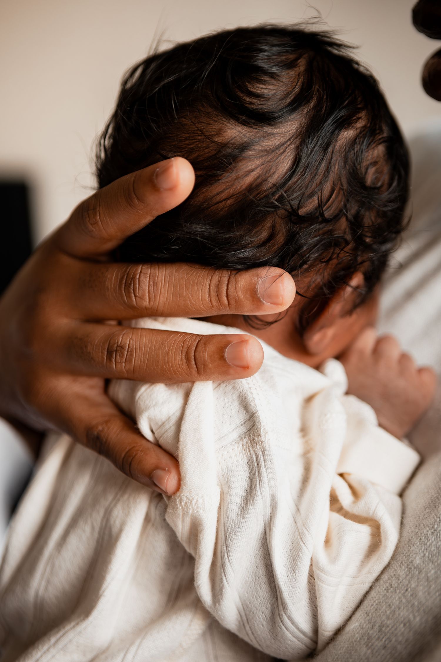 Gentle hand caresses newborn baby wrapped in white blanket during intimate moment.