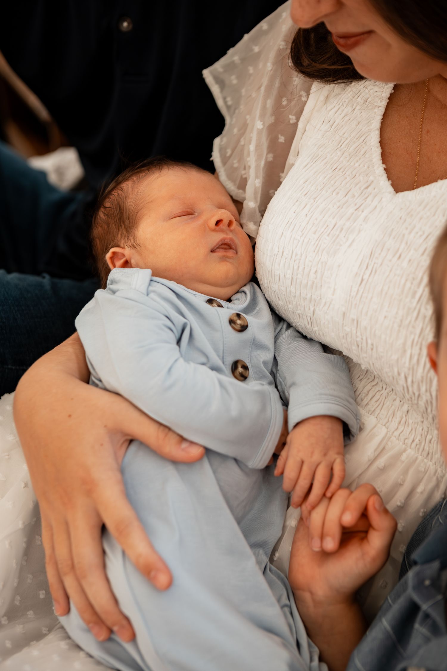 Baby dressed in light blue sleeps peacefully while being held in someone's arms.