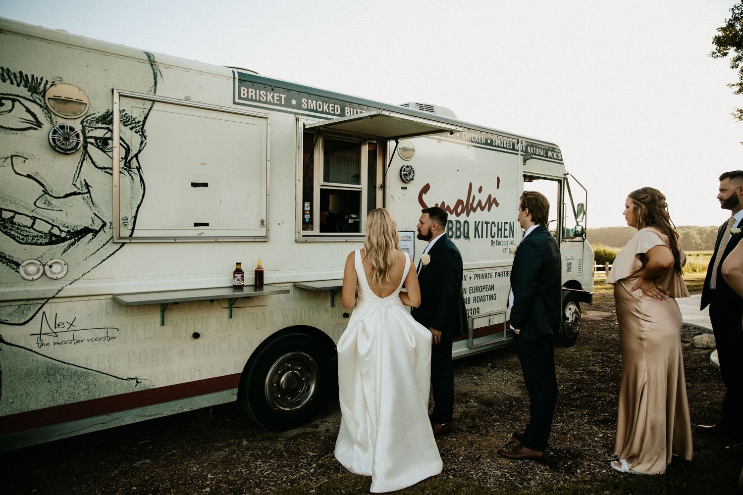 Wedding party posing and celebrating next to parked RVs at dusk.
