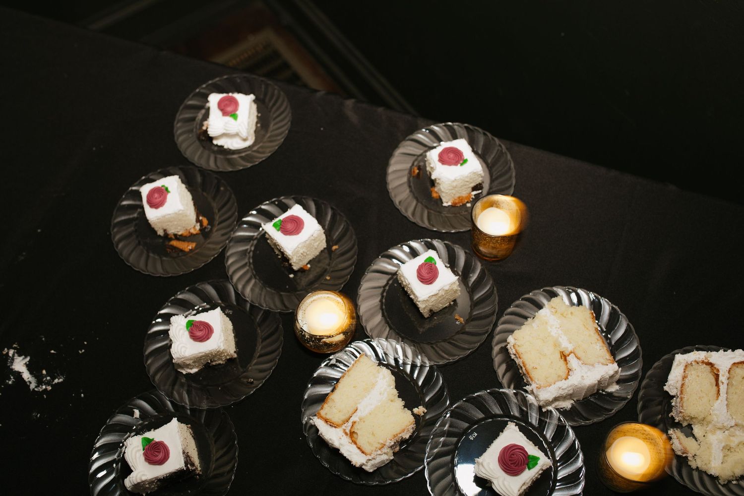 Elegant dessert plates with small cakes and candles arranged on dark plates.