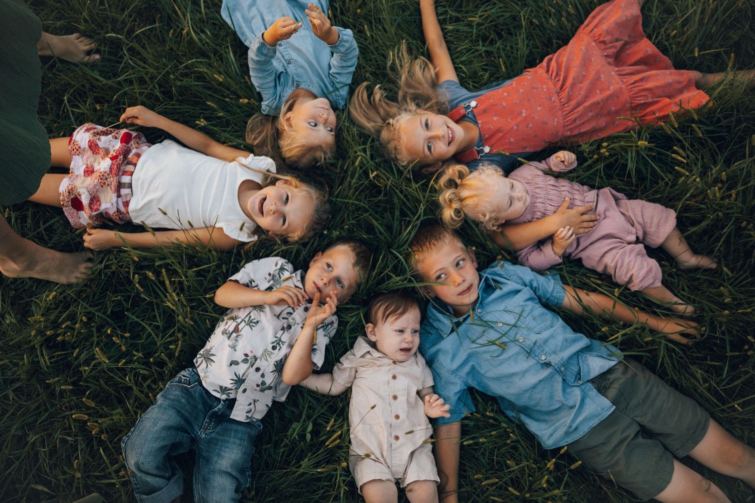 Children lying in a circle on grass making silly faces at the camera.