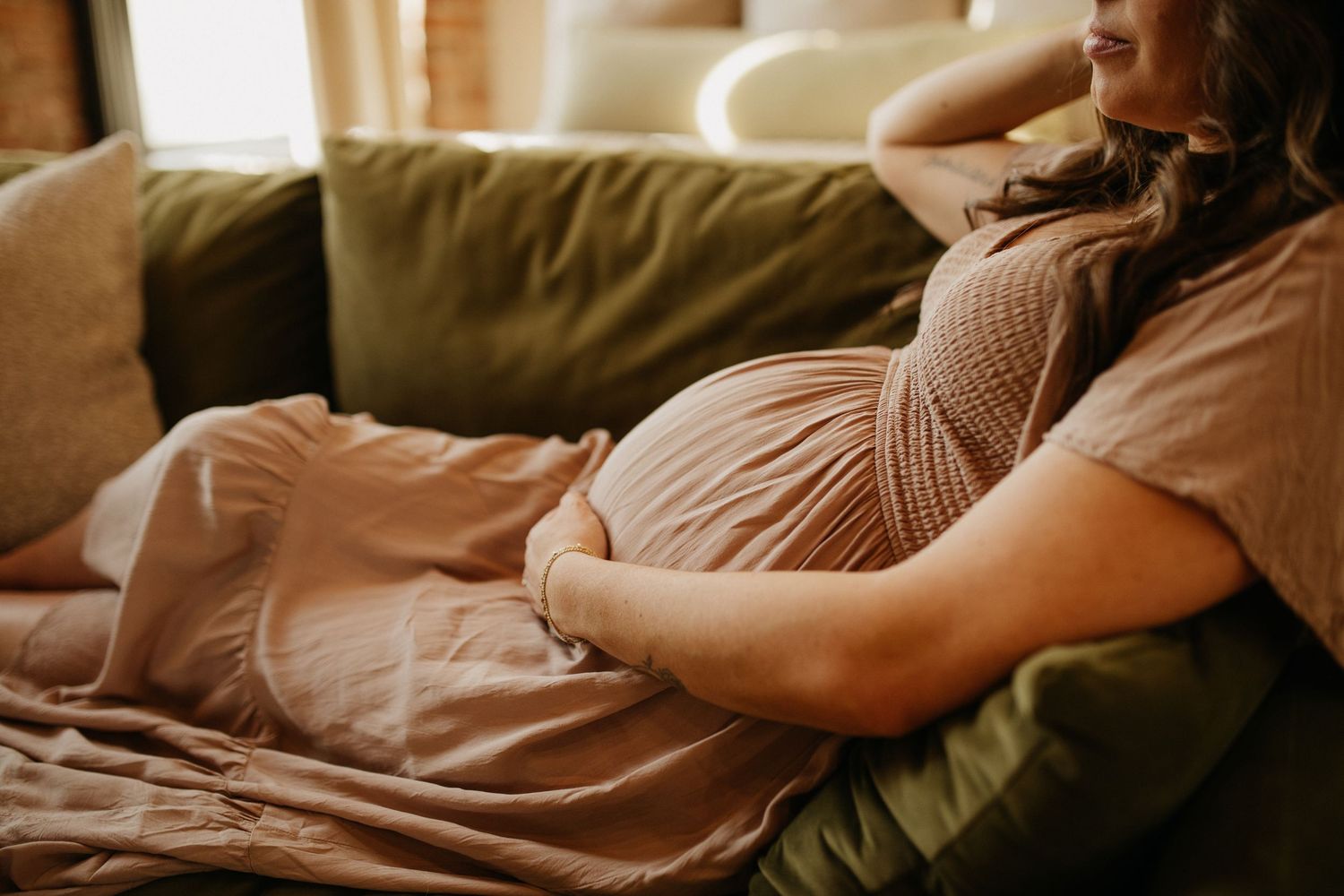 A pregnant woman relaxes on a cozy couch in soft natural lighting.