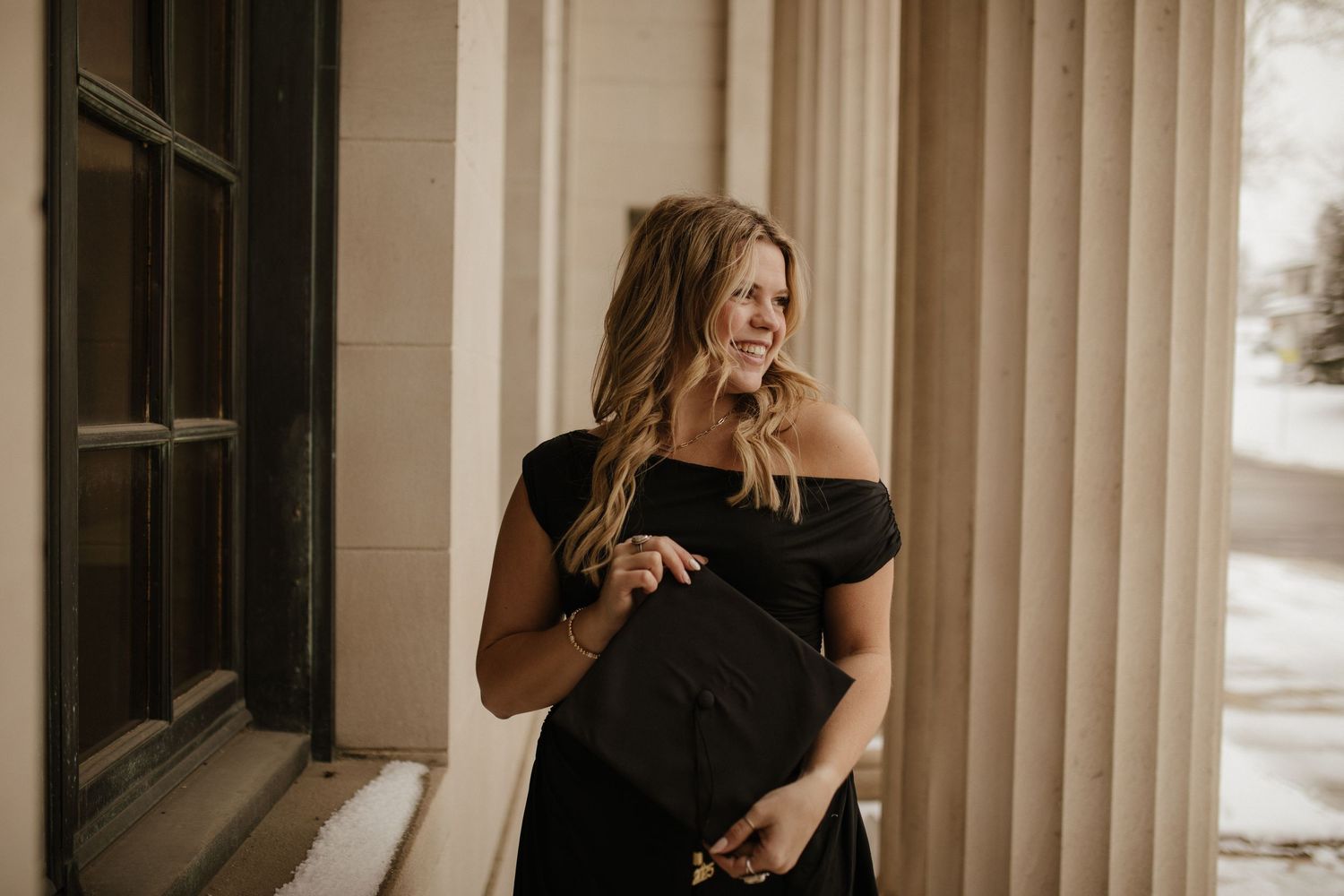 Woman in black dress posing elegantly by classic columns.